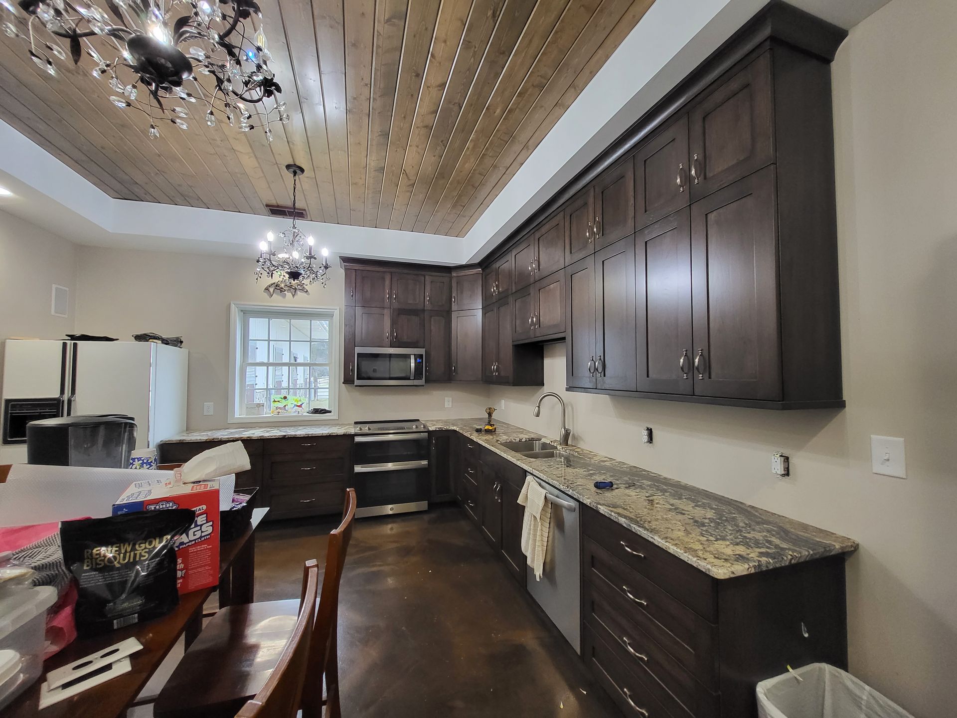 Modern kitchen with dark cabinets, granite countertops, and a wooden ceiling; cluttered table in foreground