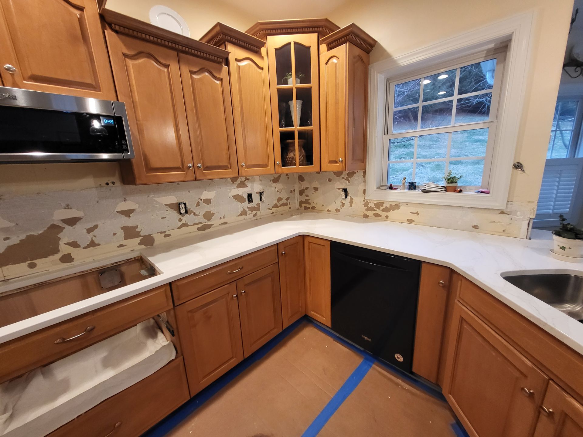 Kitchen under renovation with unfinished cabinets, exposed backsplash, and blue tape on the floor and countertop