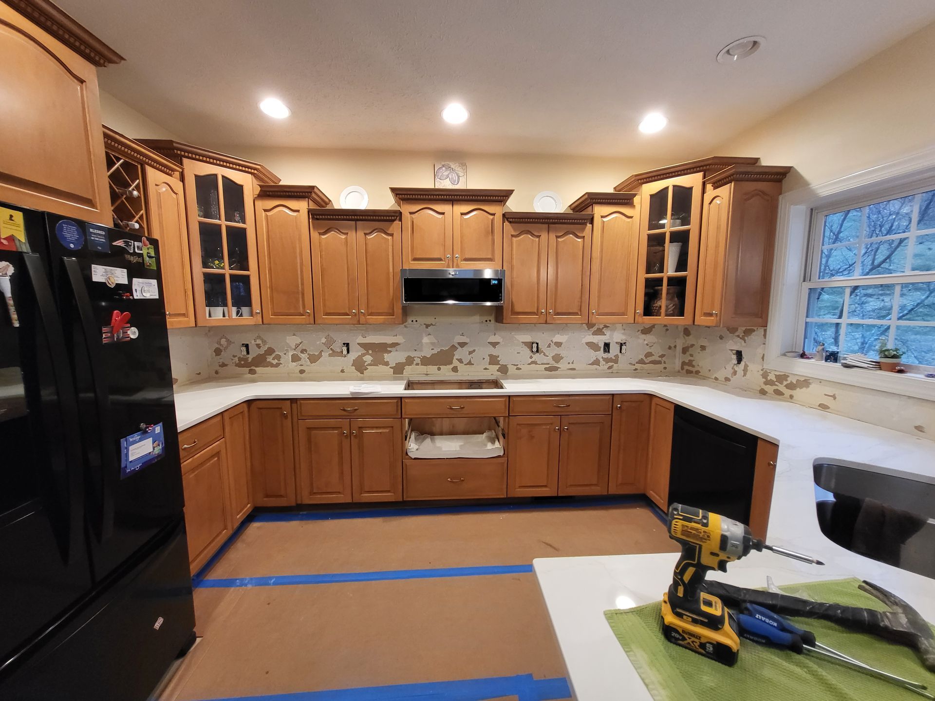 Kitchen under renovation with blue tape on the floor and a drill on the counter.