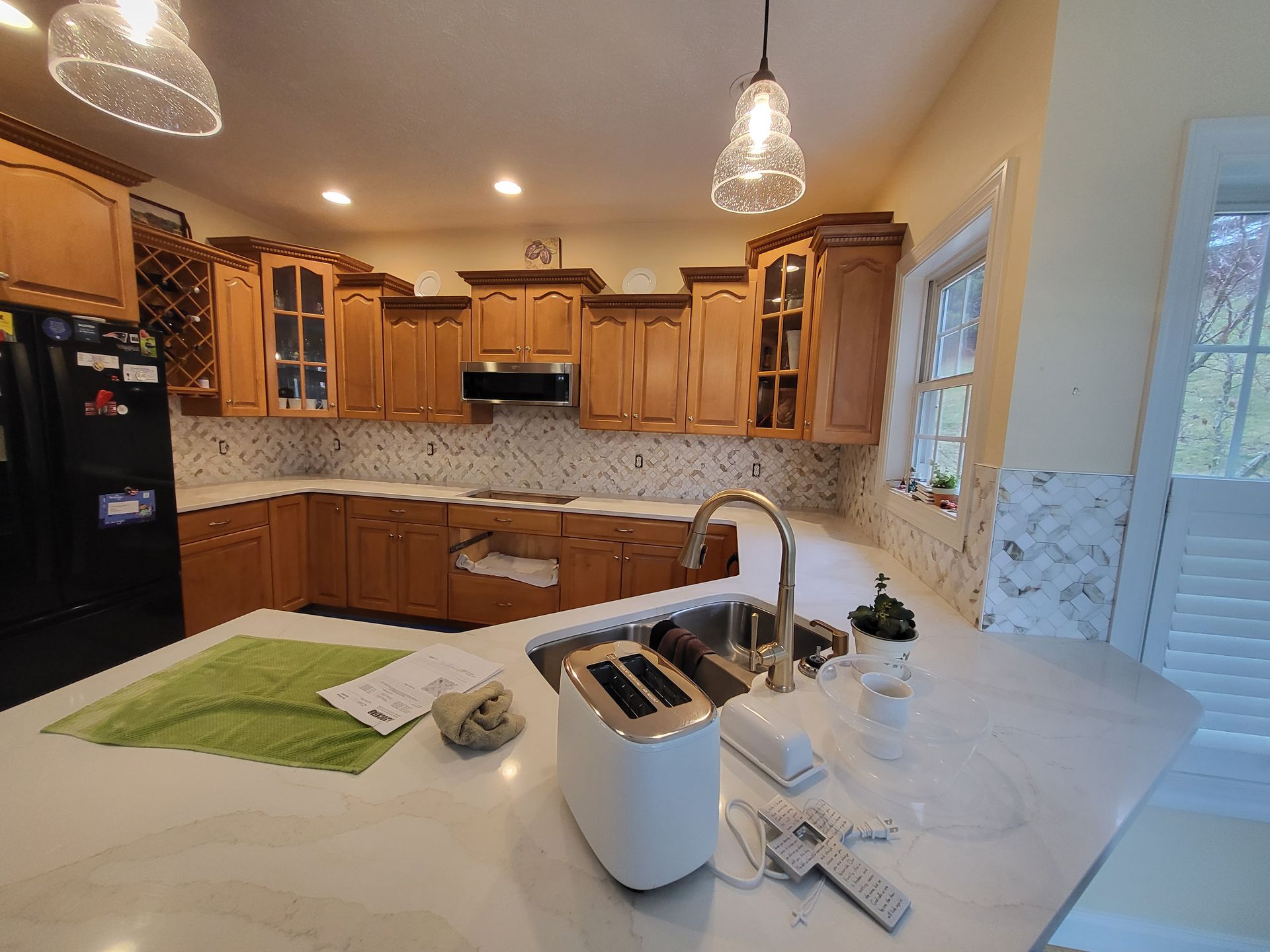 Bright kitchen with wooden cabinets, white countertops, island sink, and pendant lights