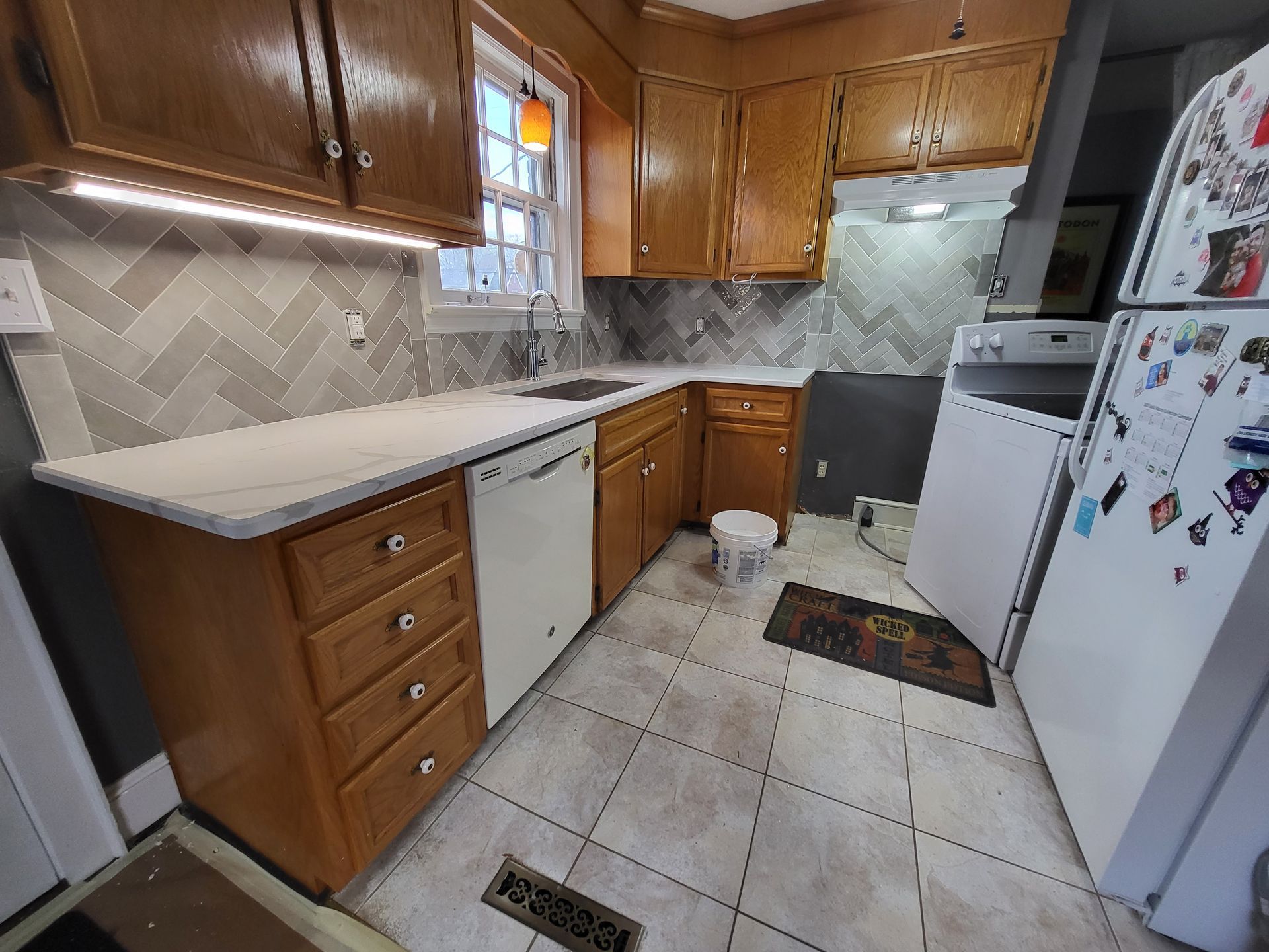 Small kitchen with wood cabinets, white appliances, tiled floor, and a window above the sink.