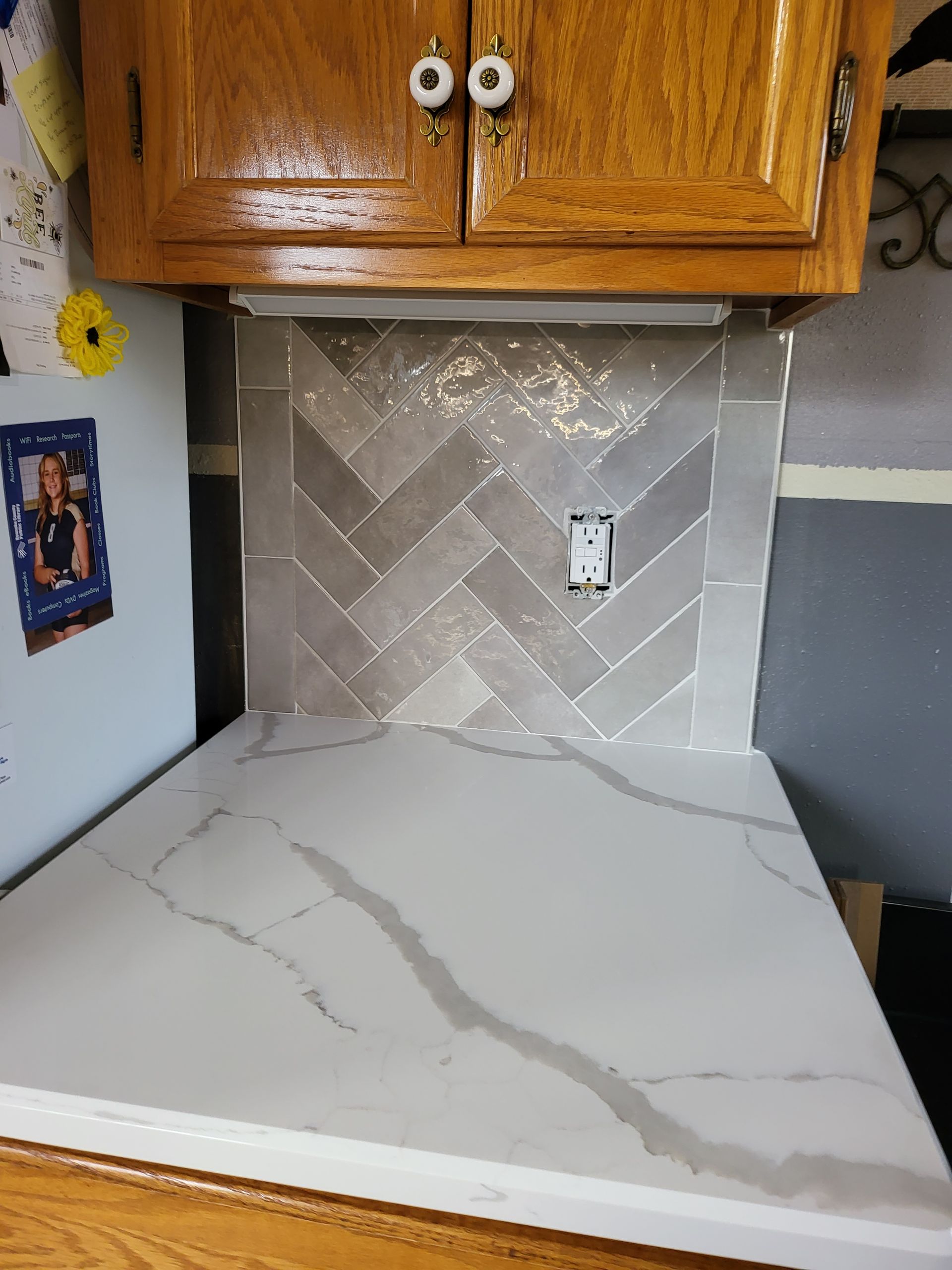 Kitchen countertop with gray marble pattern, herringbone backsplash, and wooden cabinets above