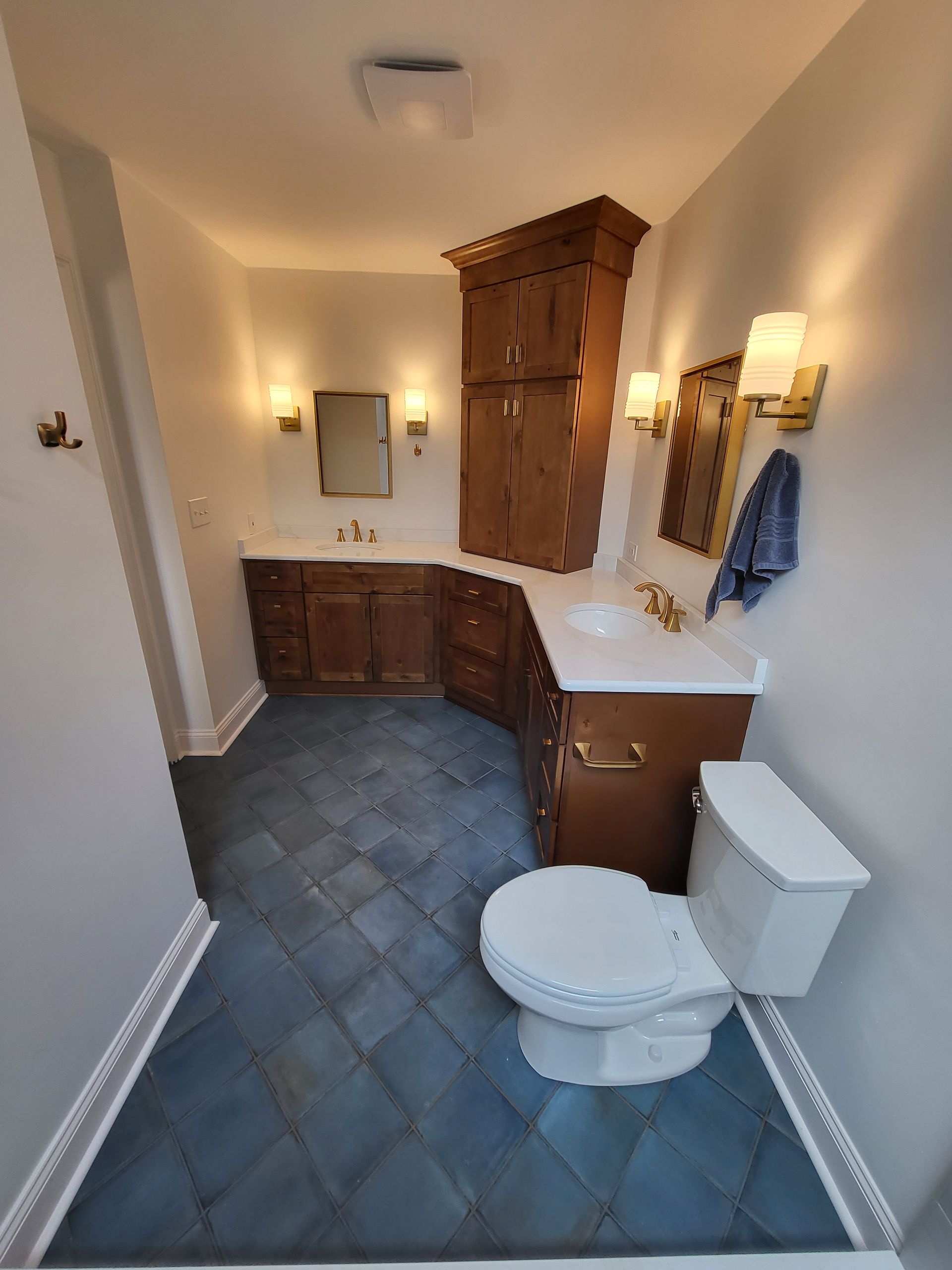 Bathroom with blue tile floor, wood cabinets, white toilet, vanity, and wall-mounted lights