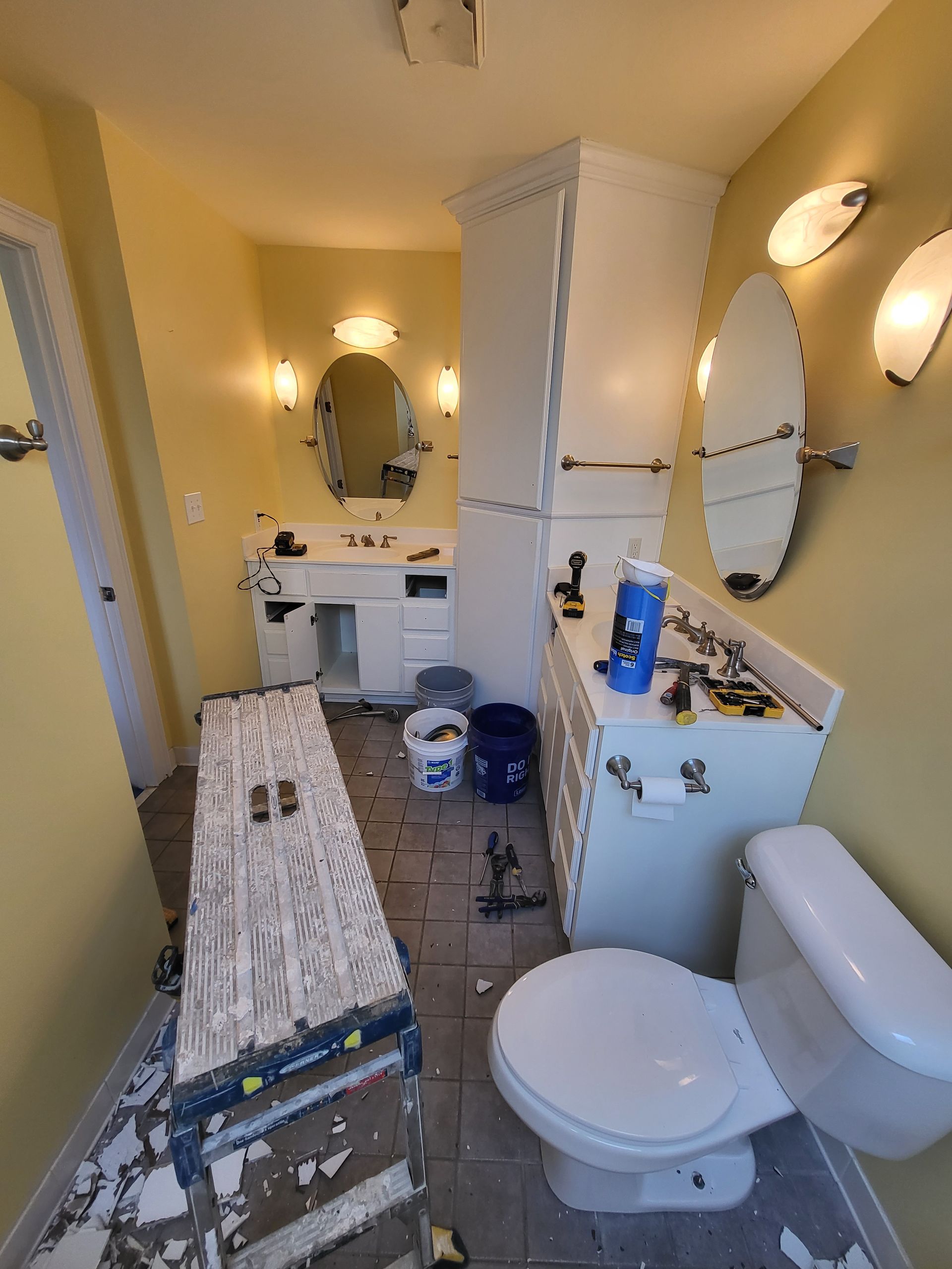 Small bathroom under renovation with vanity, toilet, ladder, and tools on the floor
