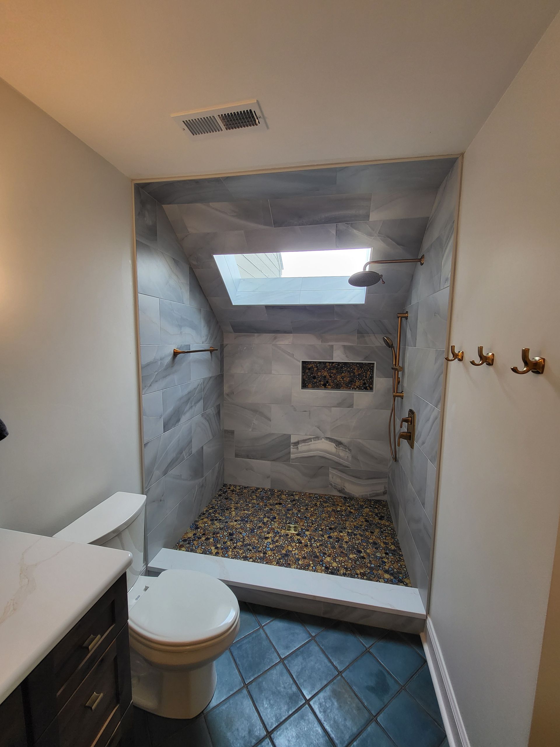Small bathroom with toilet, vanity, hooks, and unfinished tiled shower area with gravel floor.