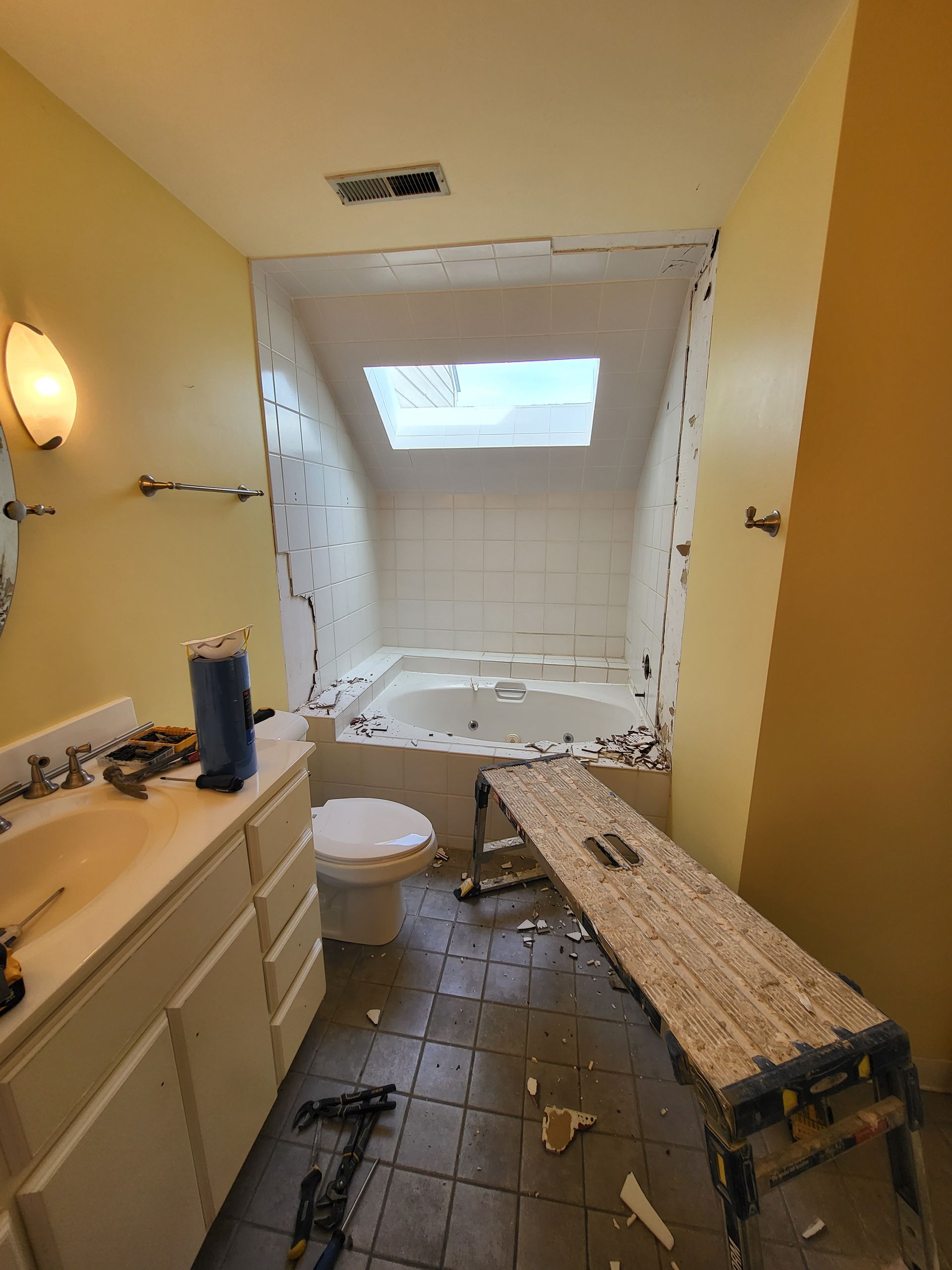 Bathroom under renovation with torn ceiling, exposed debris, and a workbench in the shower area.