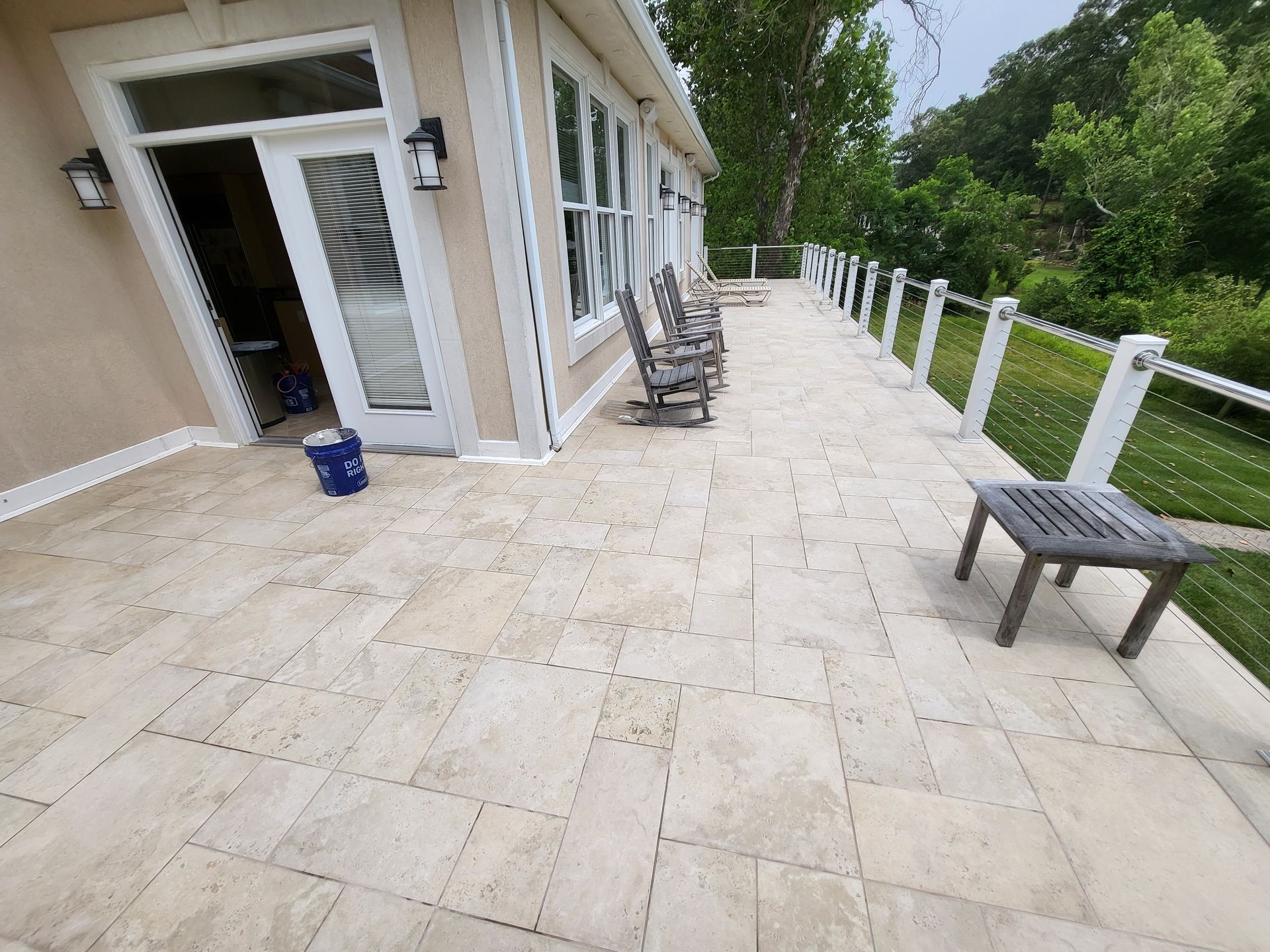Stone patio beside a house with chairs, open door, and white railing overlooking greenery