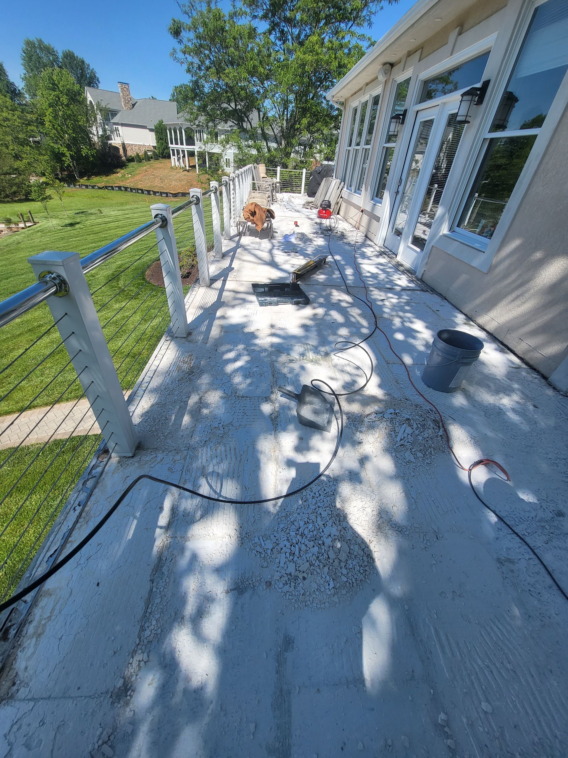 Back porch under renovation with white painted floor, railings, tools, and sunny yard beside house