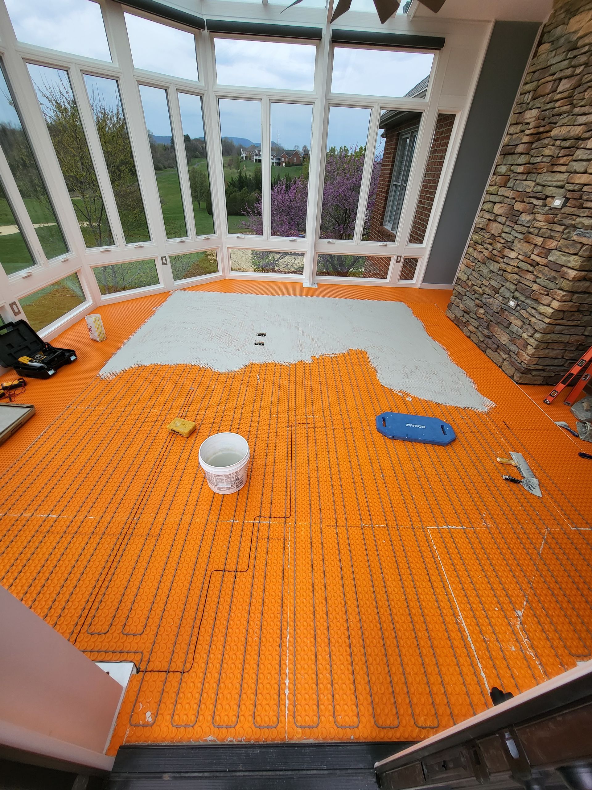 Orange flooring panels laid on a screened porch, with a bucket, tools, and a stone wall.