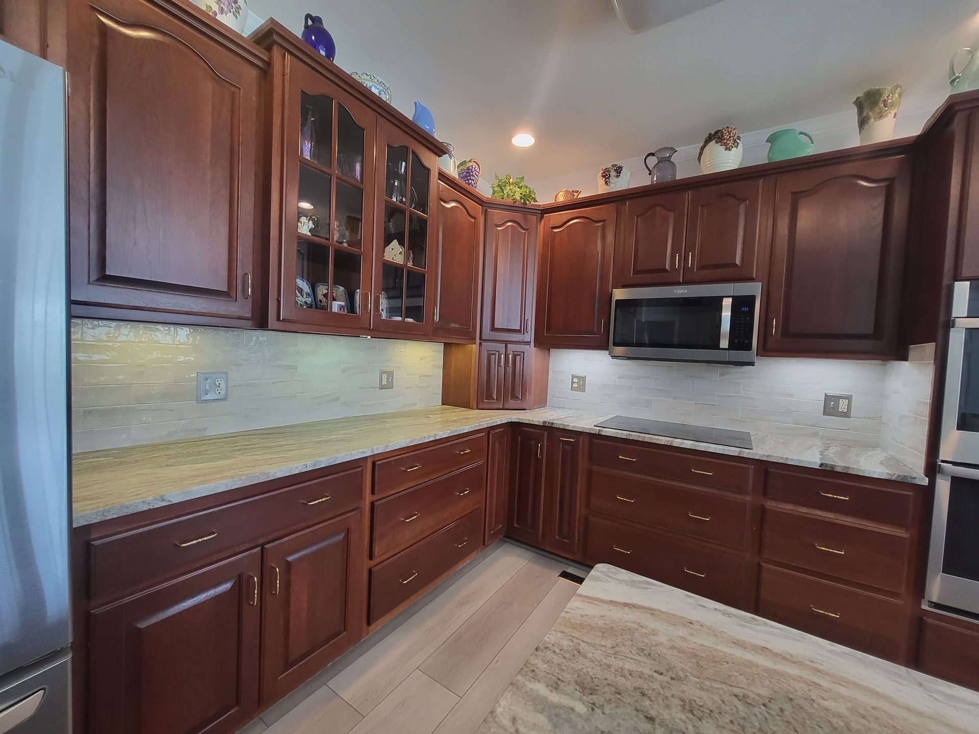 Wooden kitchen with dark cabinets, light countertops, and stainless steel microwave under bright ceiling lights