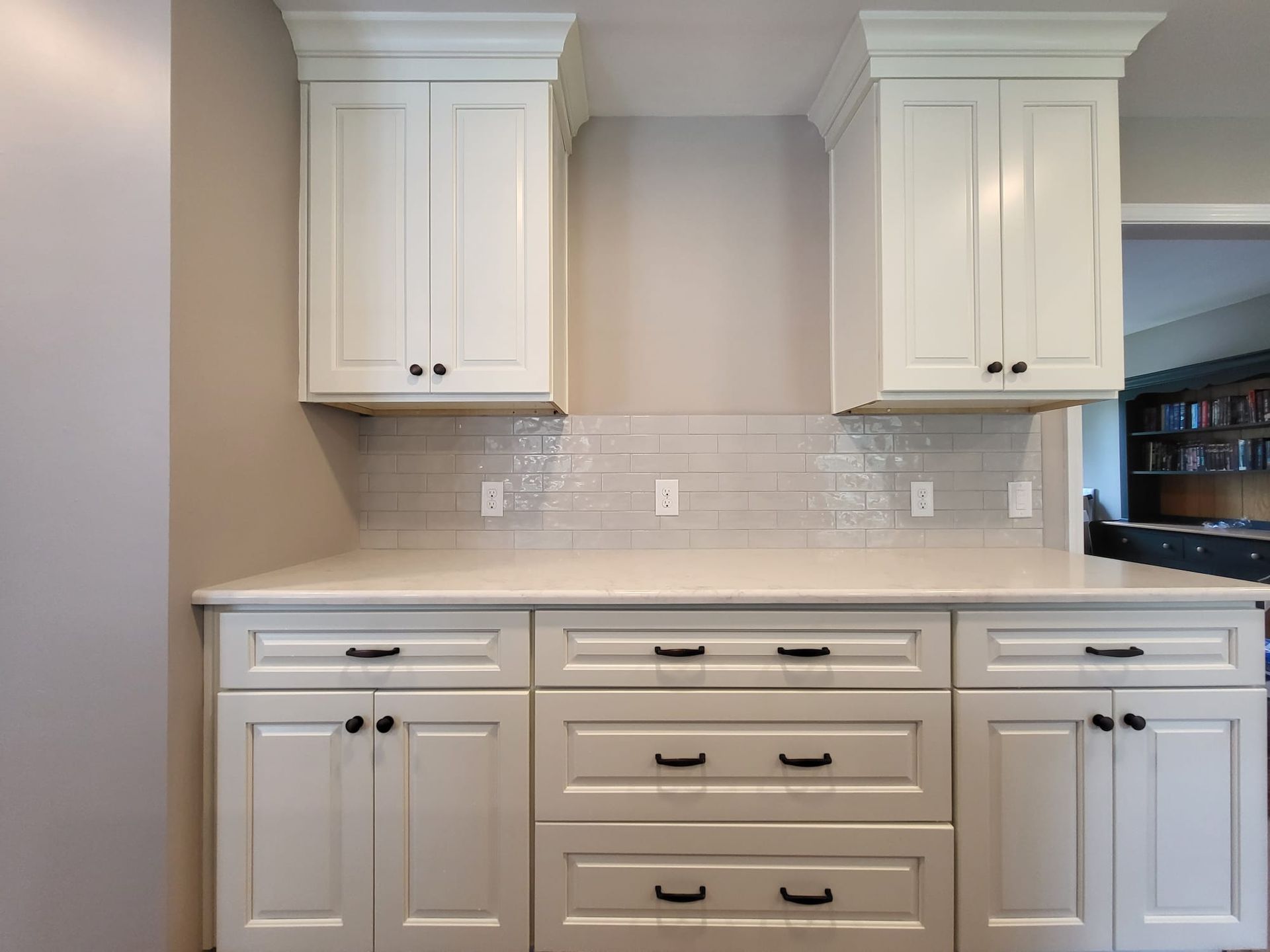 White kitchen cabinets and beige backsplash with countertop and built-in drawers beneath