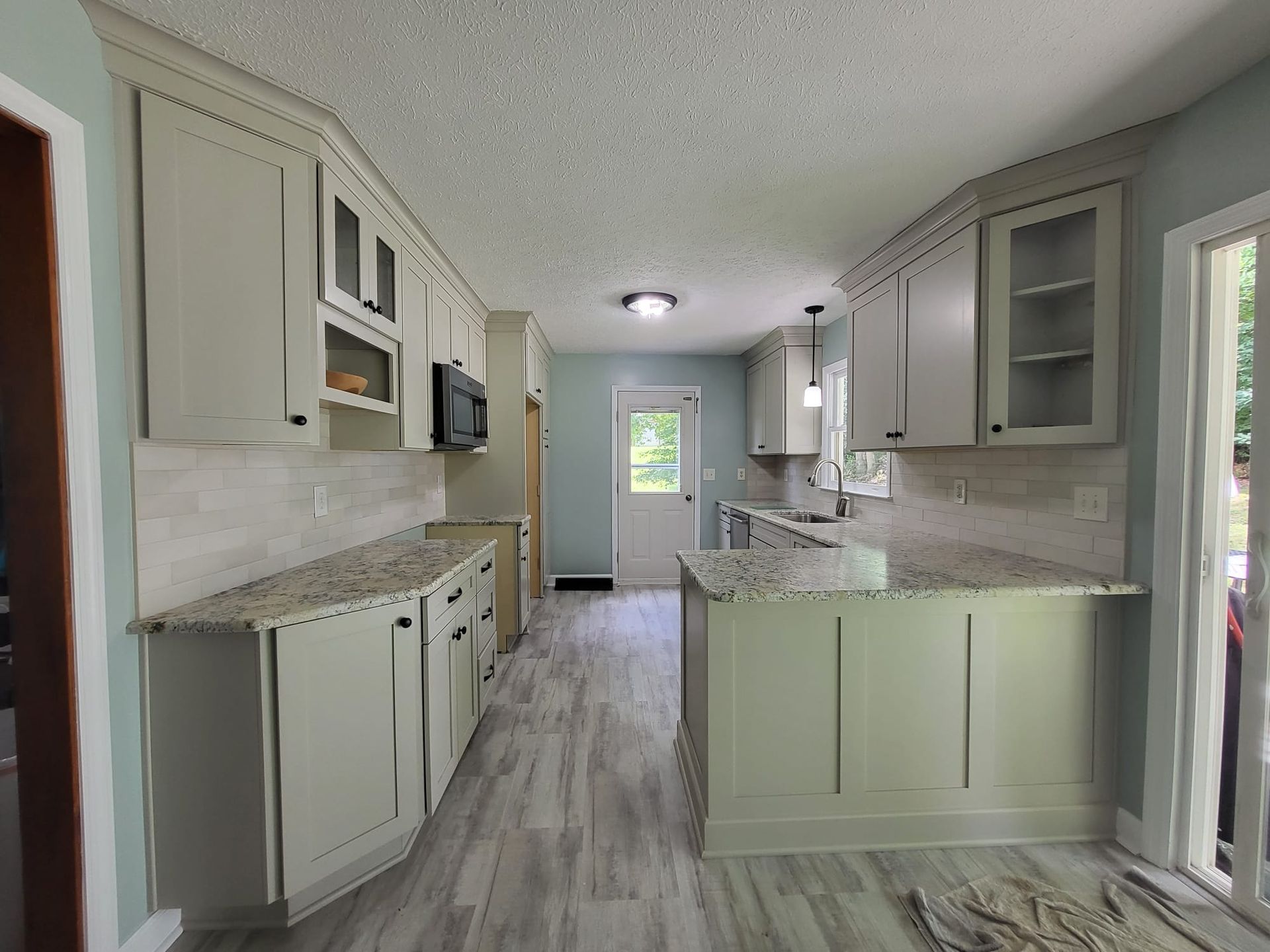 Bright narrow kitchen with white cabinets, gray countertops, and a view toward a back door
