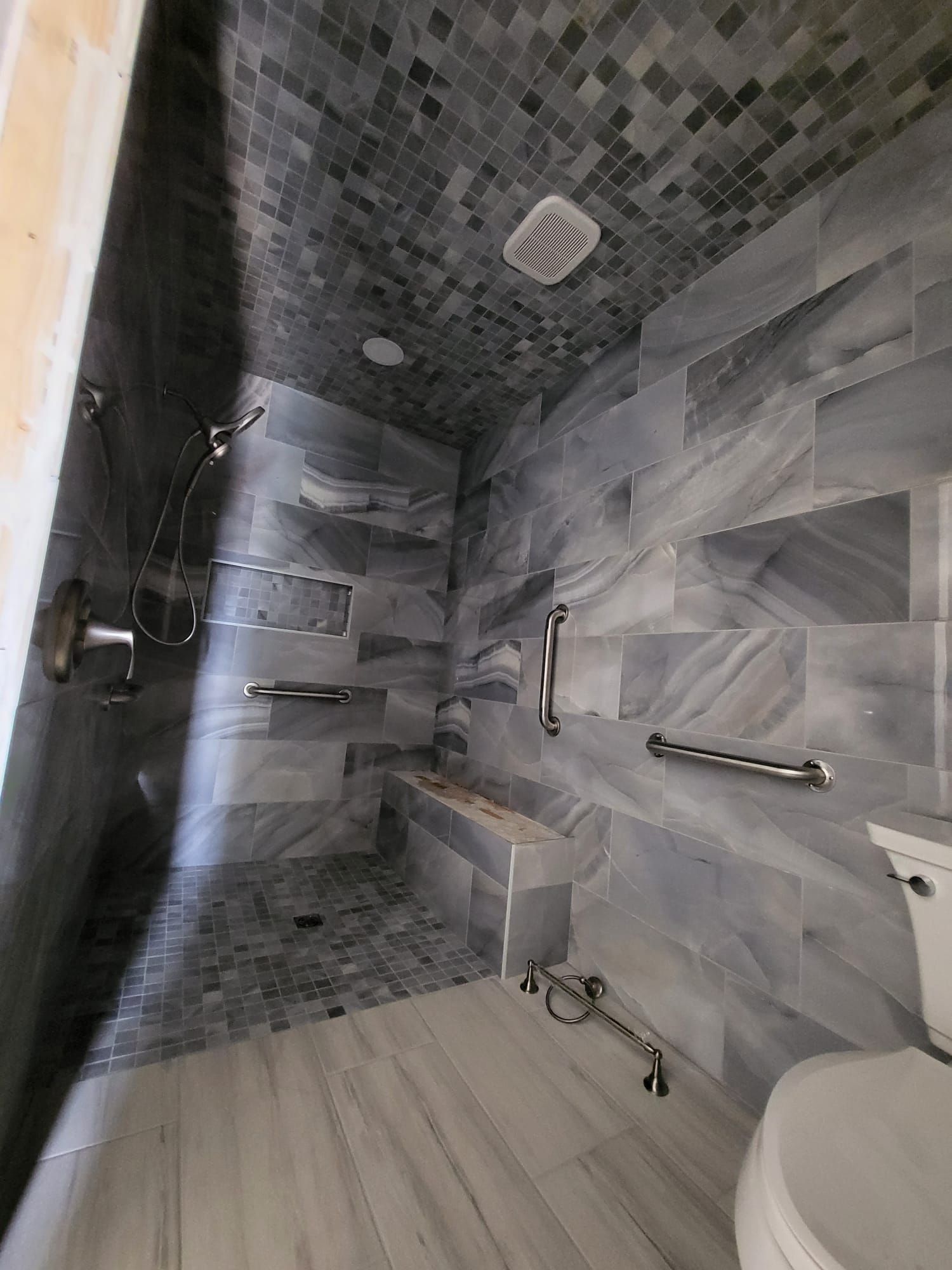 Modern tiled walk-in shower with bench, grab bars, and rainfall showerhead