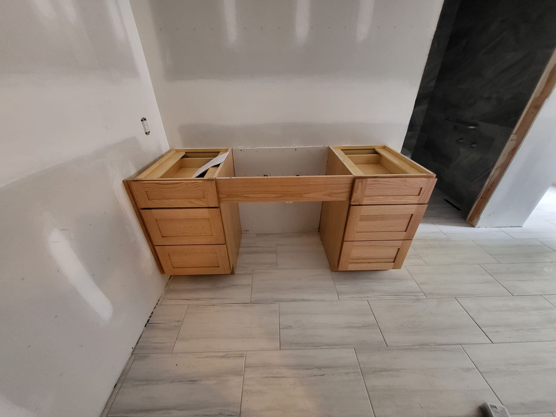 Wooden double-sink vanity cabinet under construction against a white wall on a tiled floor.