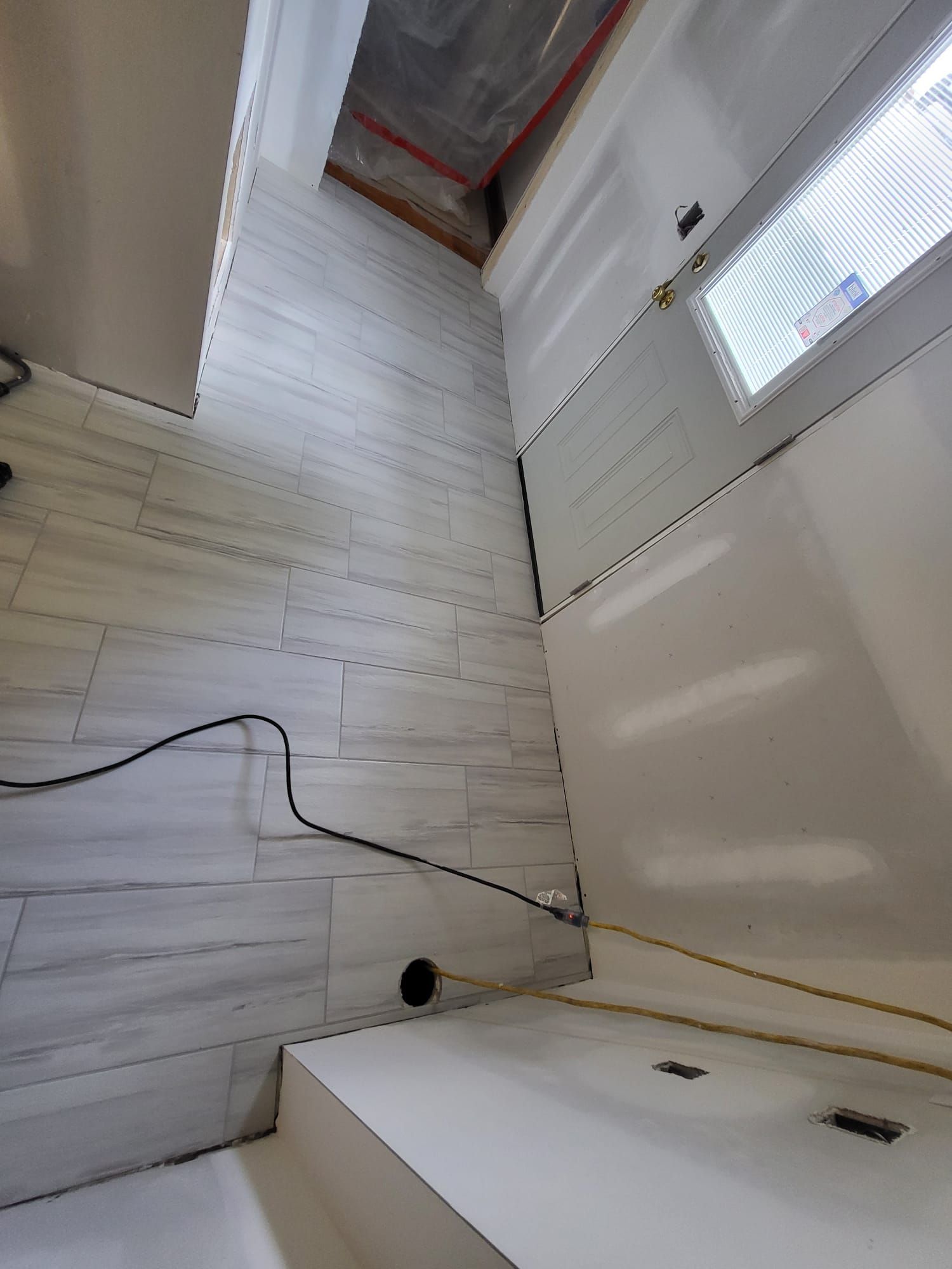 Renovation interior with white paneling, exposed ceiling, window blinds, and a black cord on the floor.