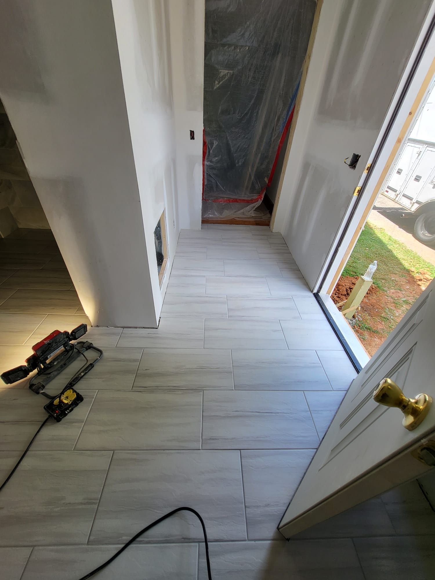 Hallway with light gray tile floor, open door, and construction tools on the left