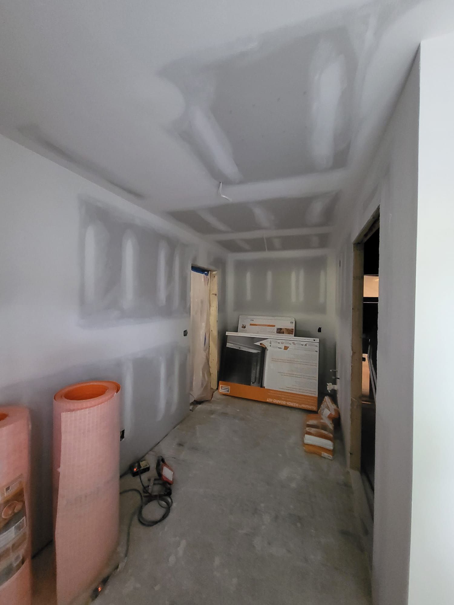 Drywalled hallway under renovation with tools, exposed floor, and a cabinet at the far end.