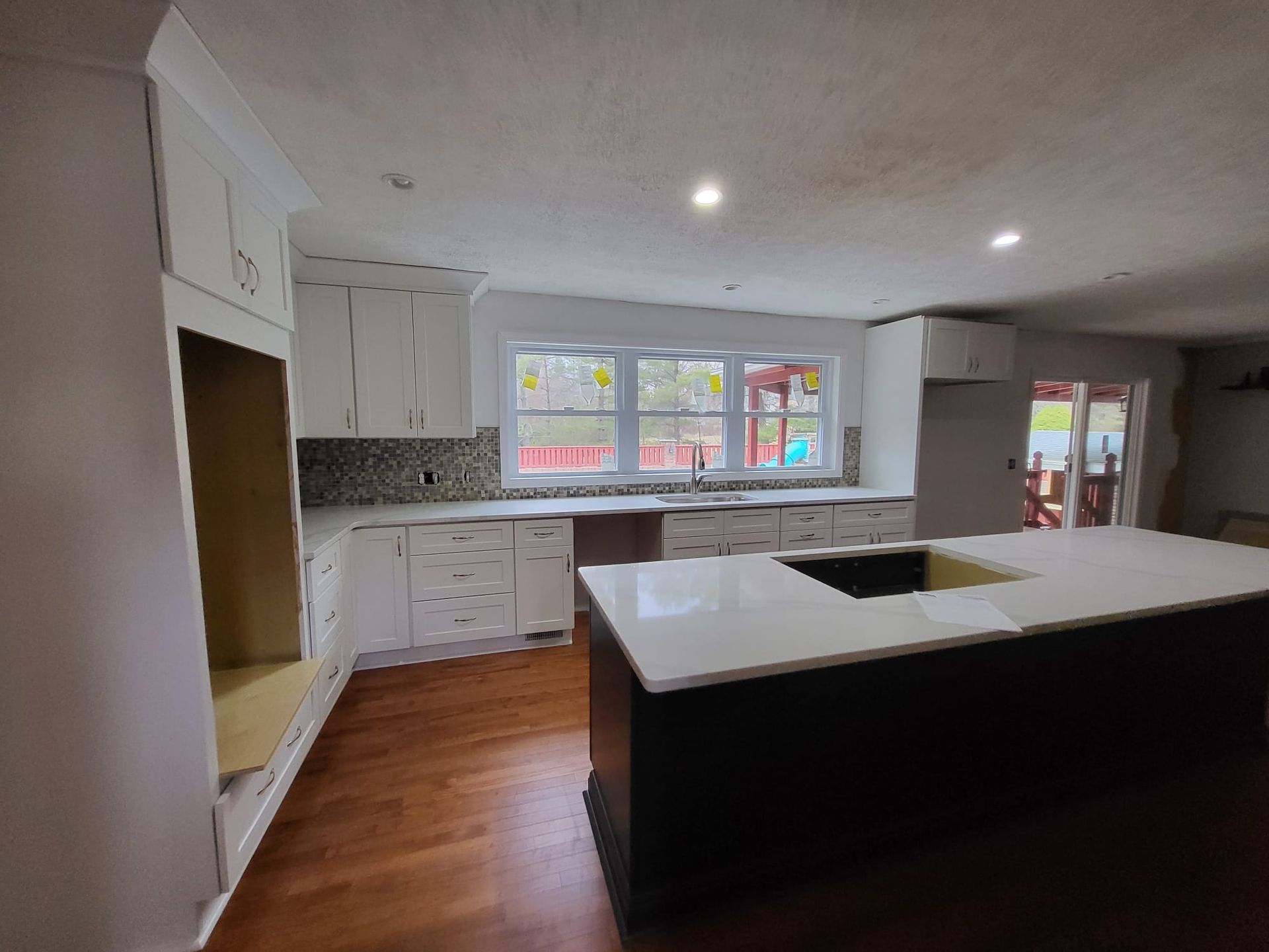 Bright kitchen with white cabinets, wood floors, a large island, and windows overlooking the yard.