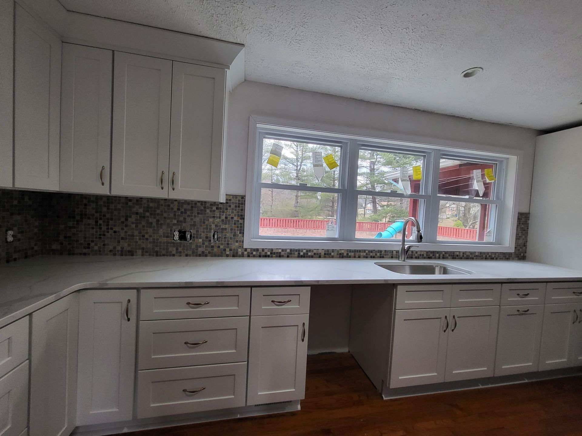 White kitchen with cabinets, mosaic backsplash, and a large window over a long countertop.