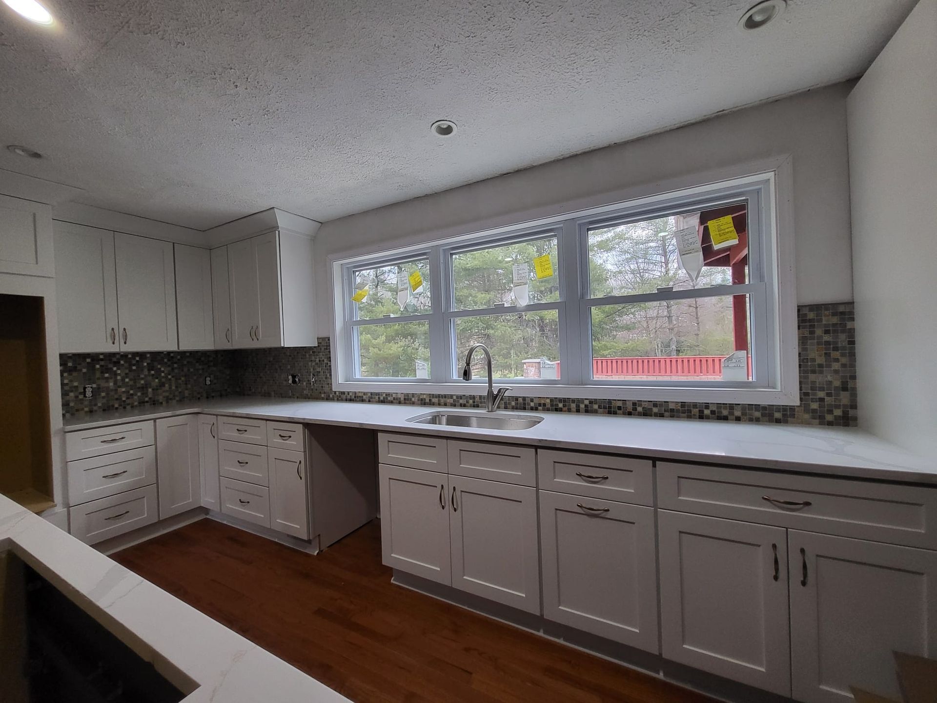 Empty modern kitchen with white cabinets, dark countertop, and large window above the sink.