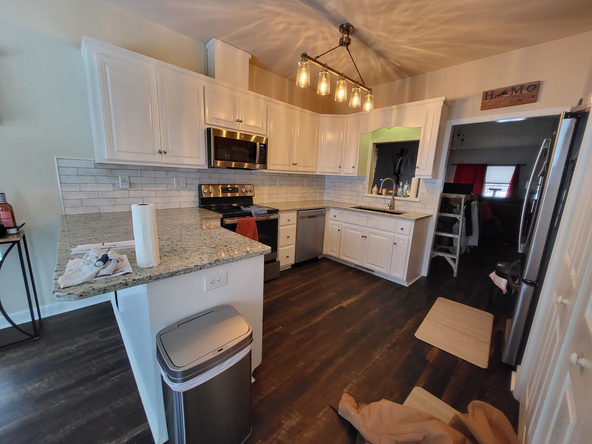 Bright modern kitchen with white cabinets, granite counters, dark wood floor, and hanging pendant lights