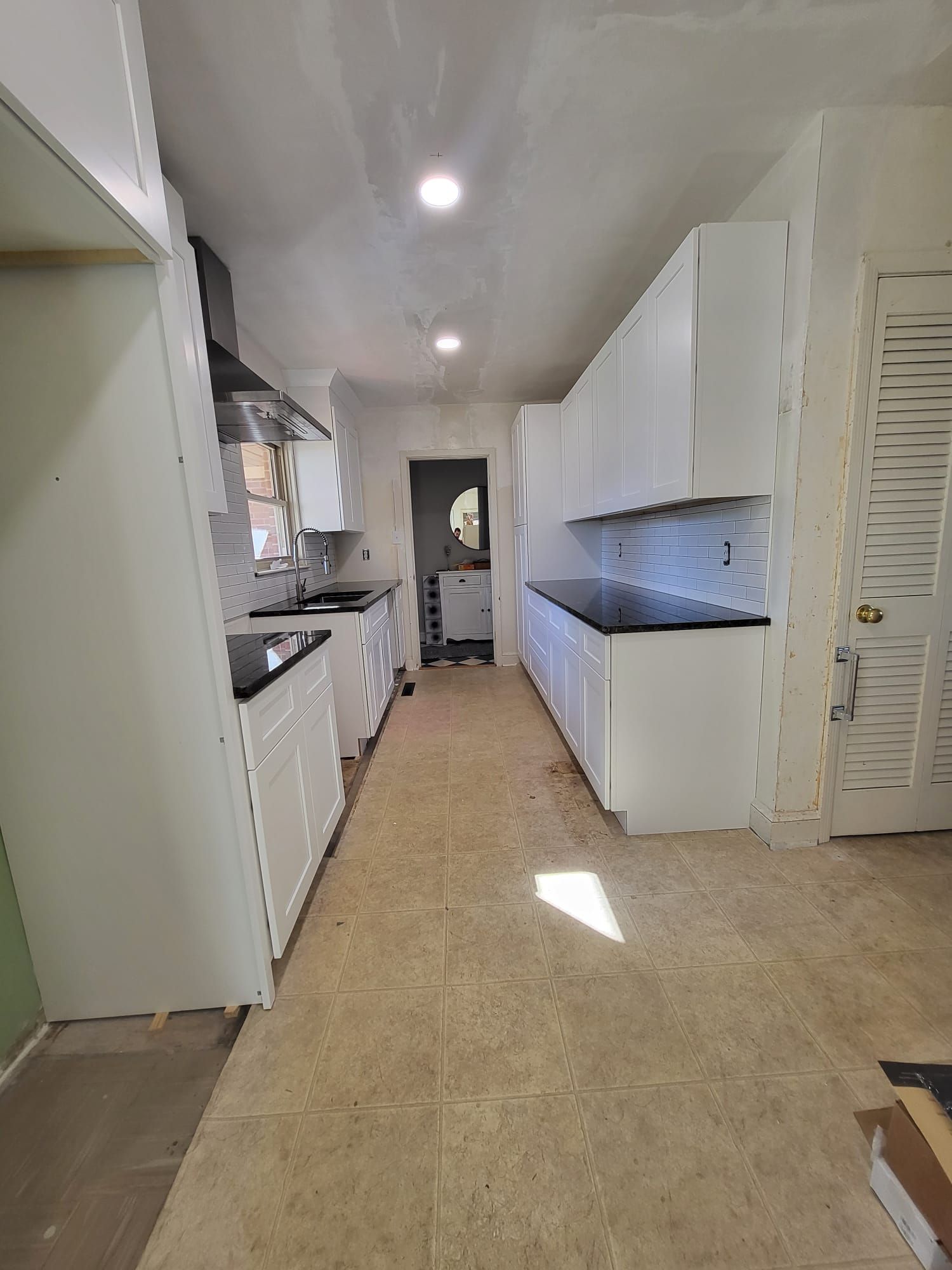 Narrow white kitchen with long counters, beige floor, and ceiling lights, viewed from the doorway