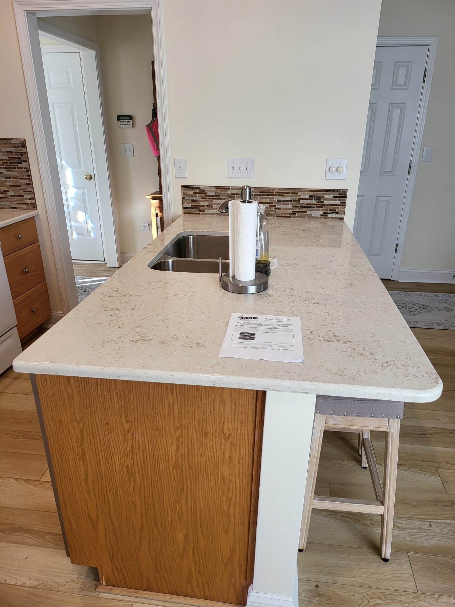 Kitchen island with speckled countertop, sink, paper towel holder, and a stool in a bright room.