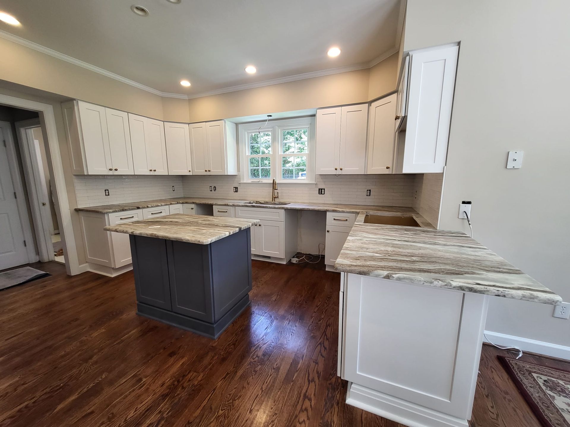 Spacious kitchen with white cabinets, granite countertops, dark wood floors, and a central island with dark base.