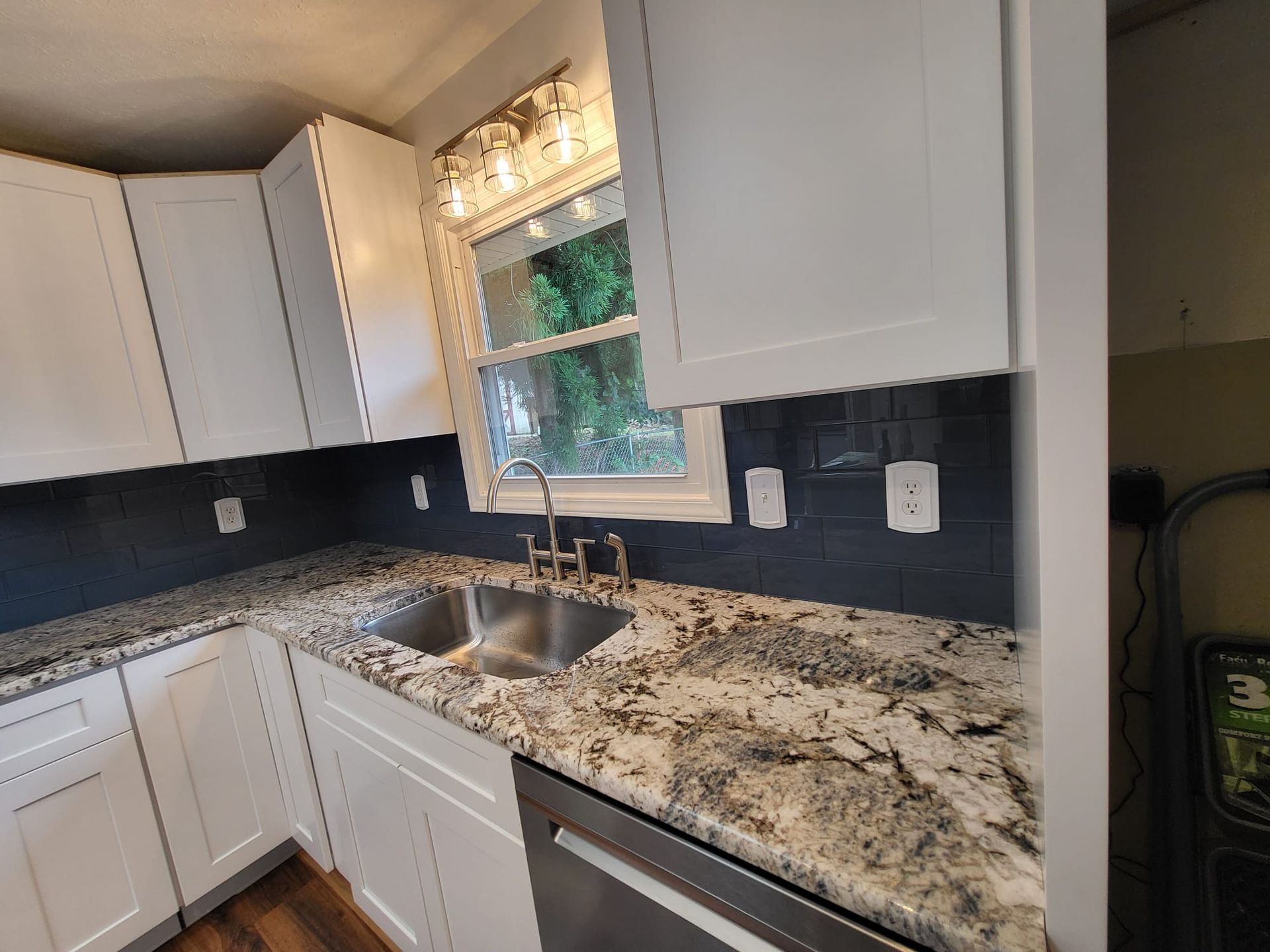 Bright kitchen with white cabinets, speckled granite counters, black backsplash, and a window over the sink.