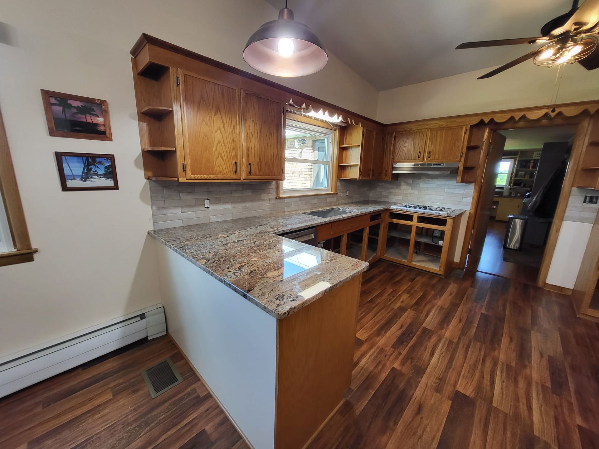 Empty kitchen with wood cabinets, granite counters, hardwood floor, and hanging light.