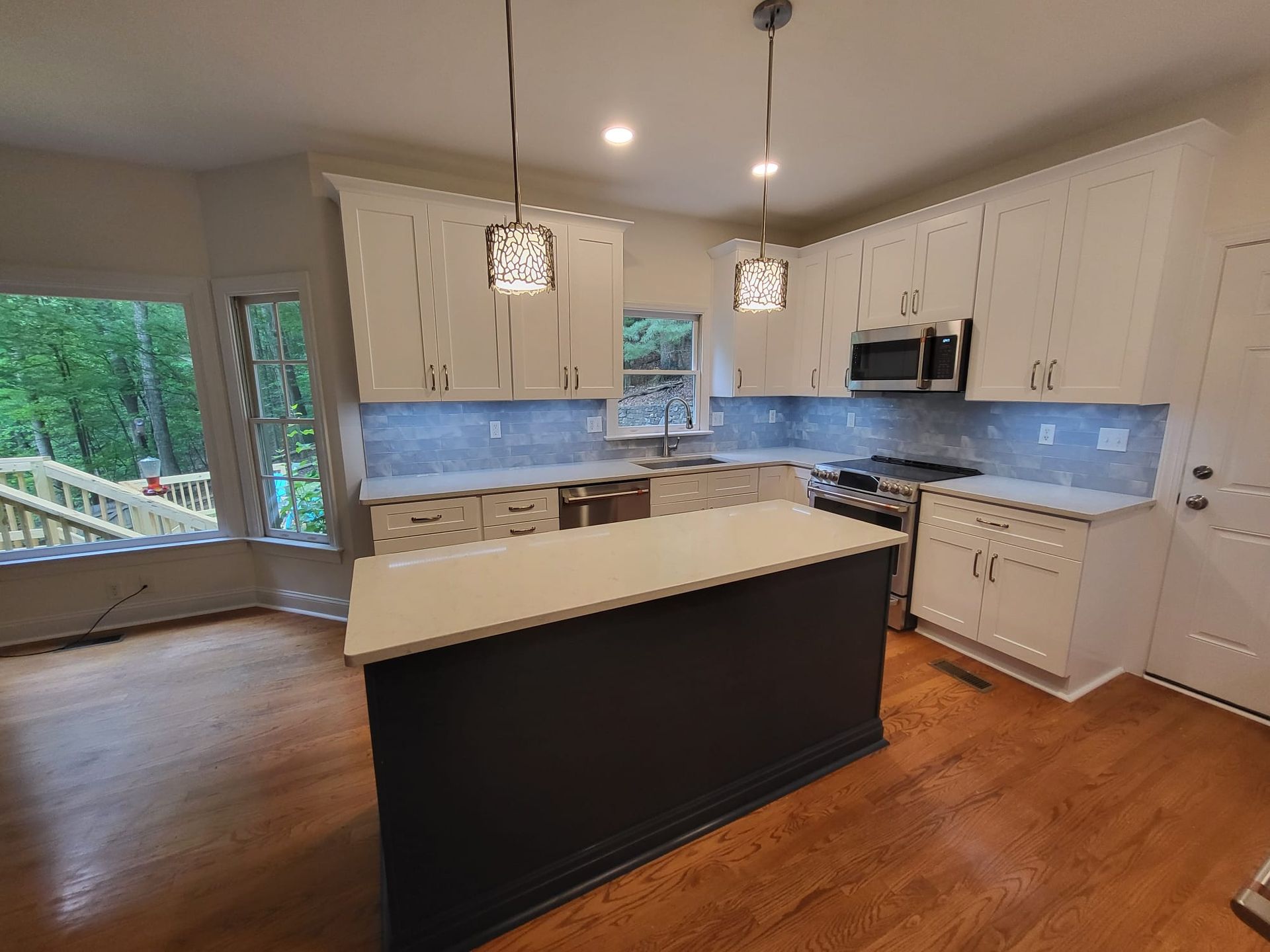 Bright modern kitchen with white cabinets, blue backsplash, black island, and hardwood floors
