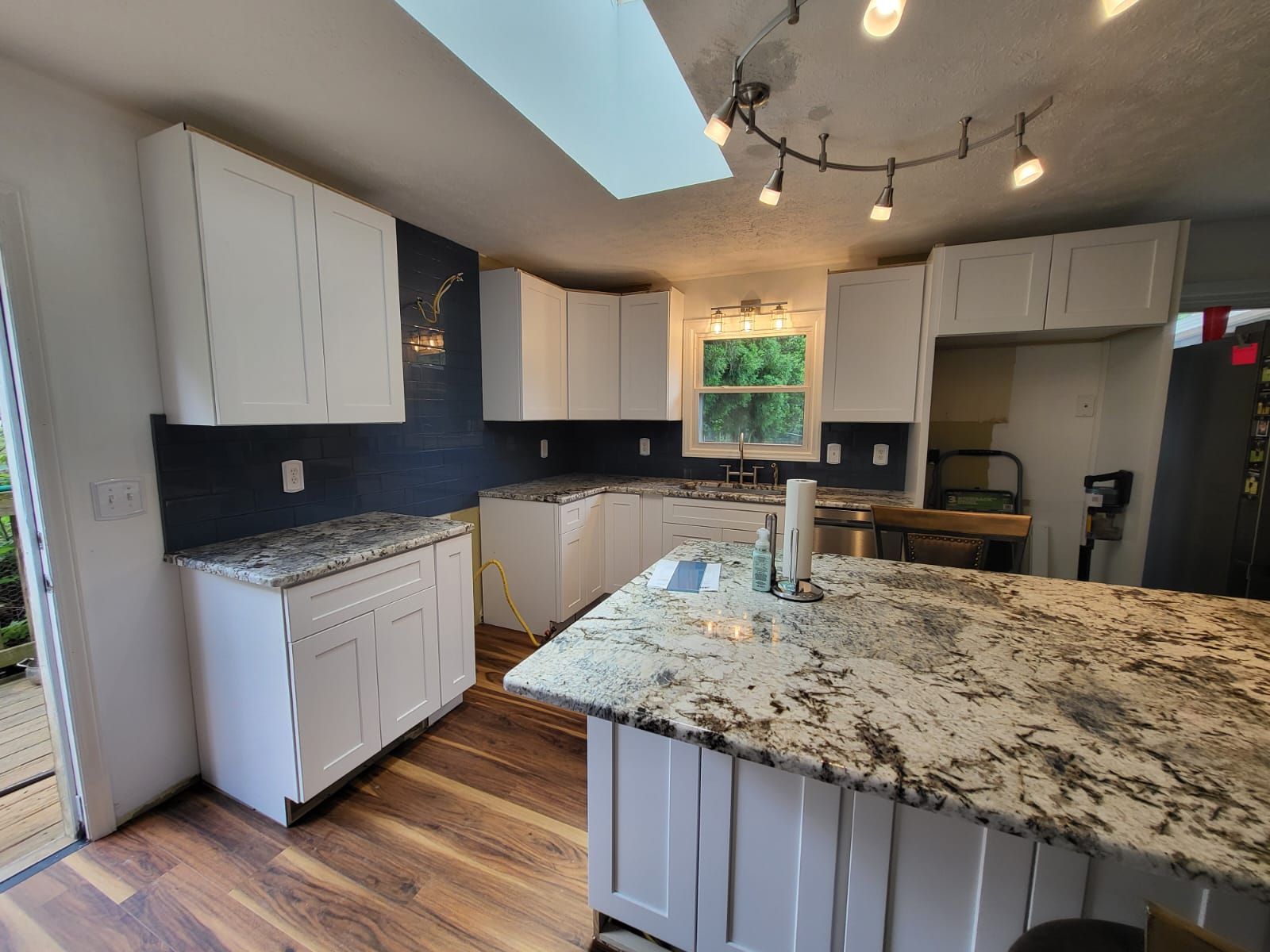 Bright modern kitchen with white cabinets, granite island, wood floors, and skylight track lighting
