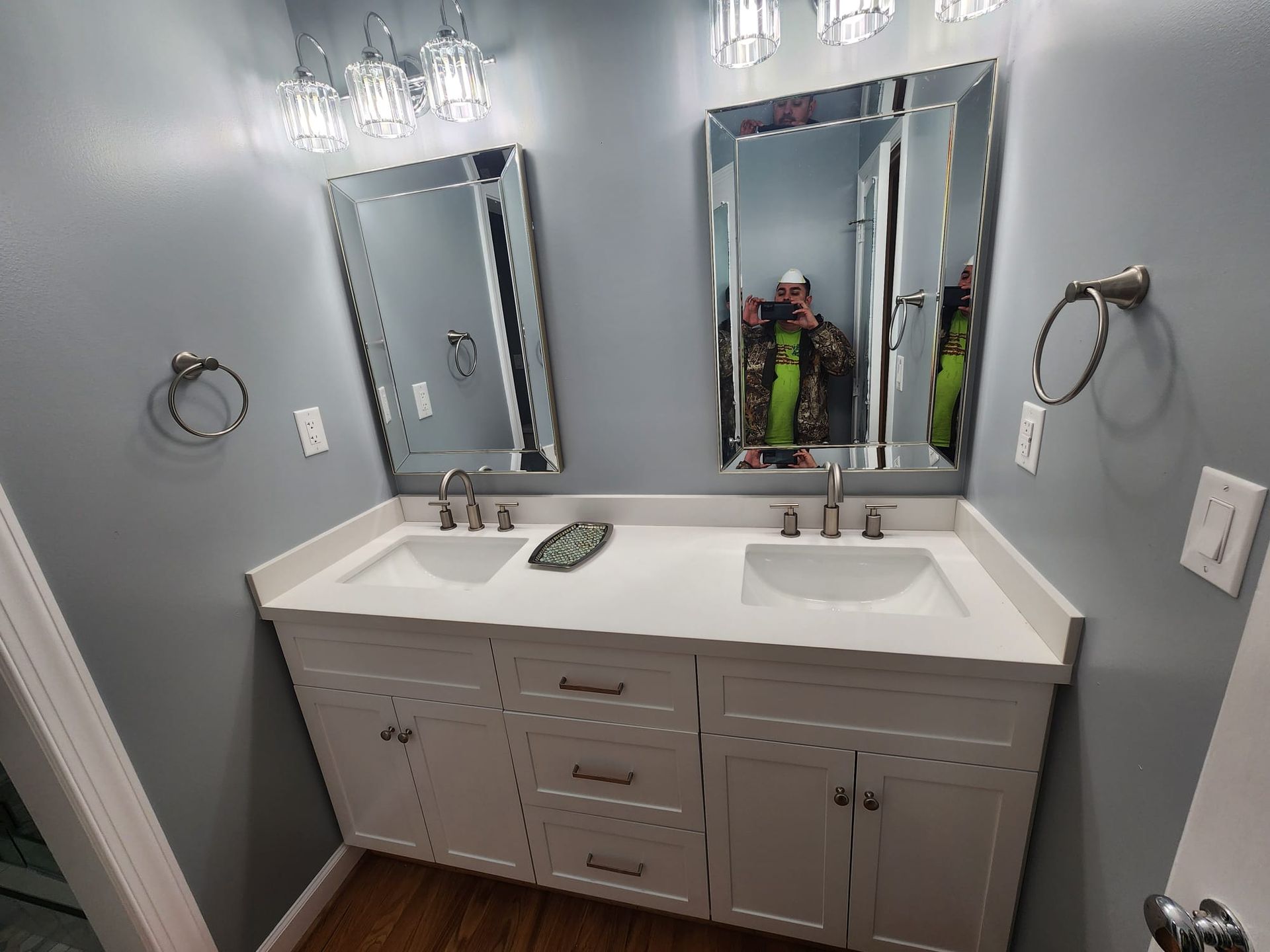 Gray bathroom vanity with double mirrors, white countertop, and chrome fixtures under a chandelier.