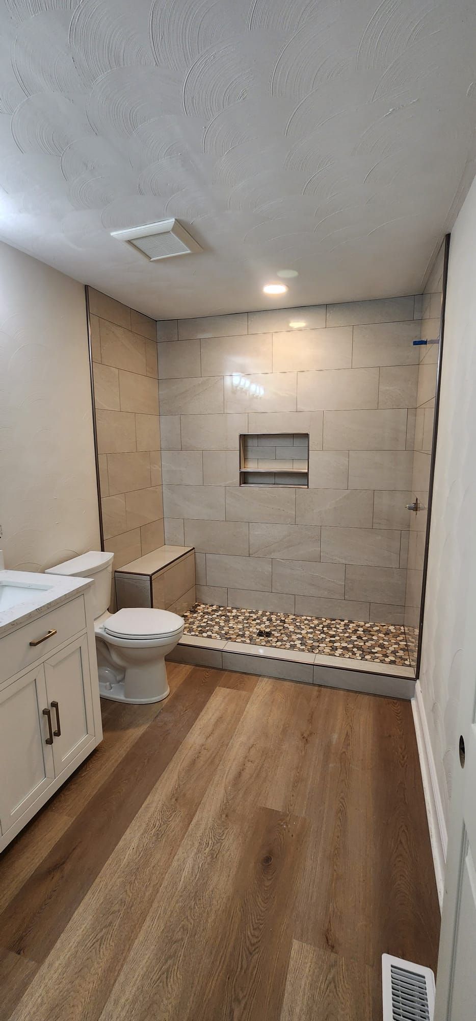 Small unfinished bathroom with toilet, shower, wood floor, and exposed cinder block walls