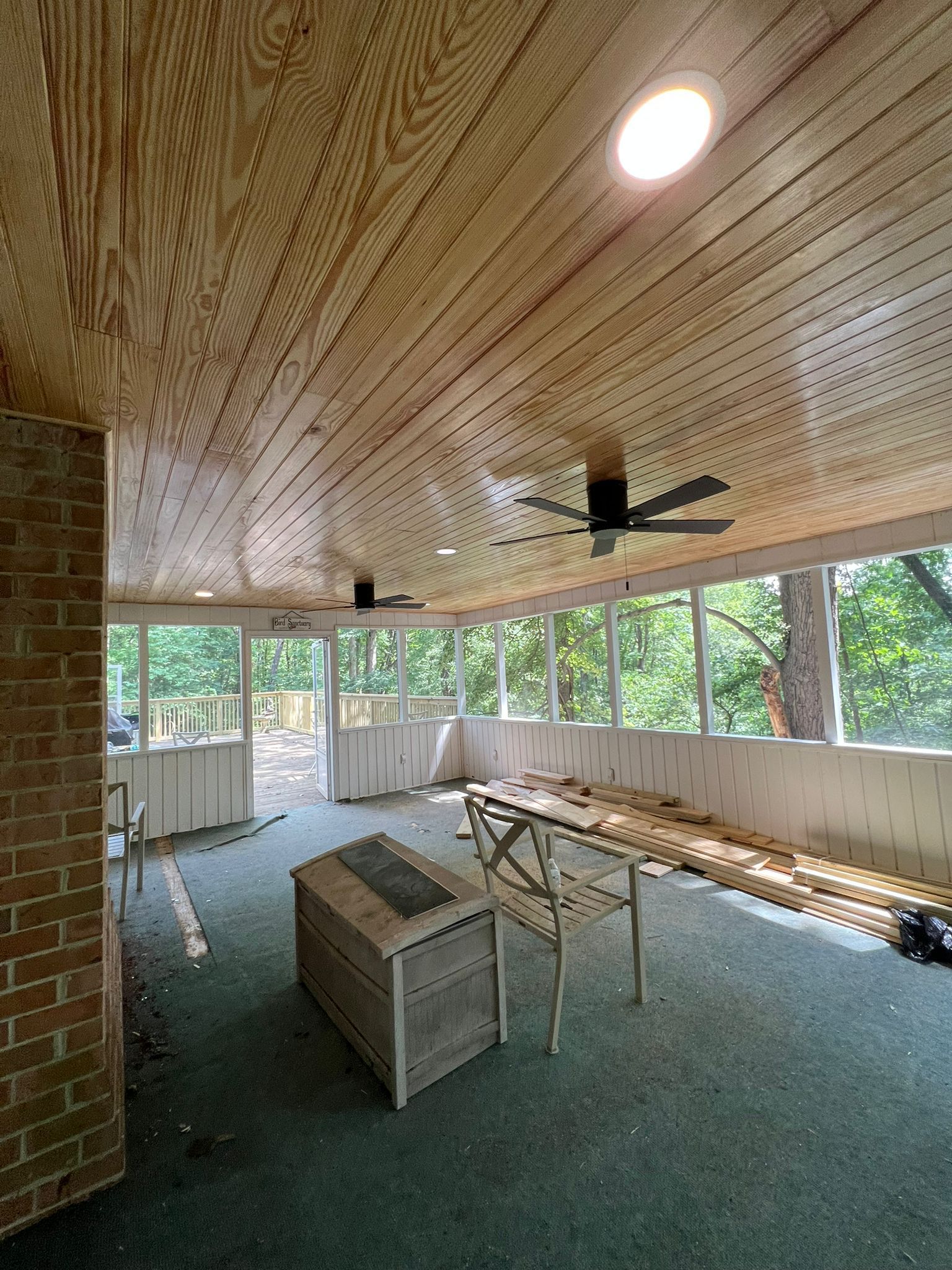 Enclosed screened porch with wood ceiling, ceiling fan, bench seating, and a central table.