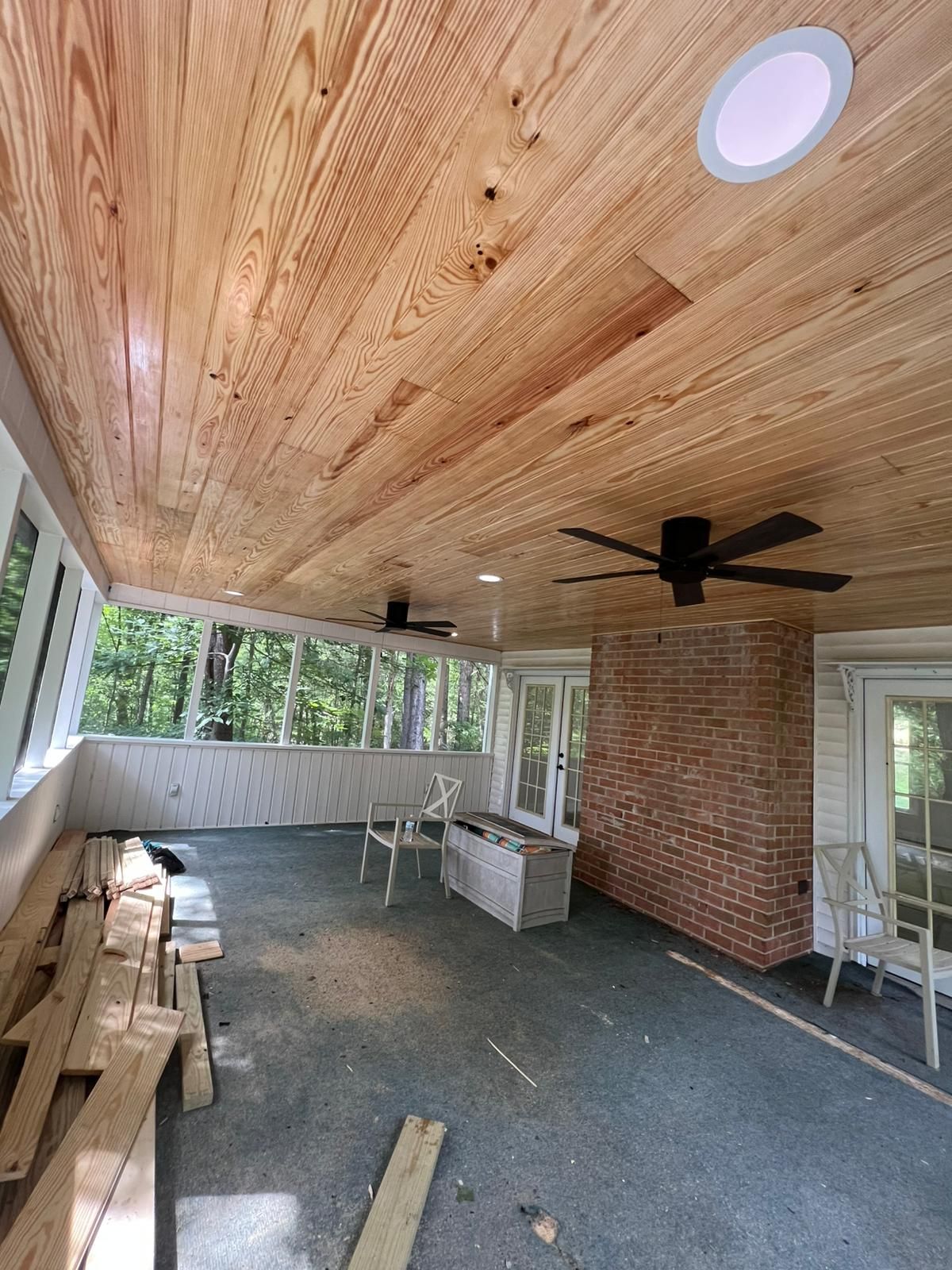 Covered porch with wood ceiling, brick wall, ceiling fan, and stacked lumber along the side.