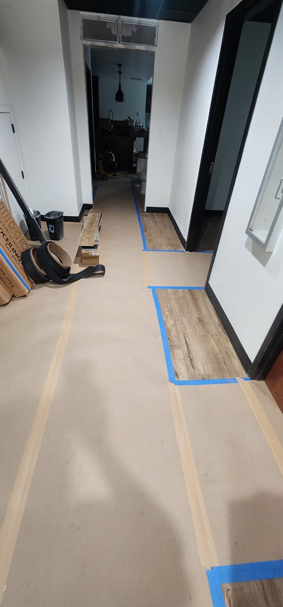 Narrow hallway with beige floor, blue tape markings, and shoes and bags along the left wall.