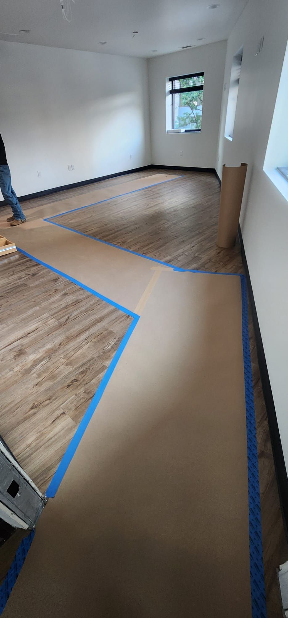 Empty room with hardwood floor and blue tape marking a walkway around a brown floor cover