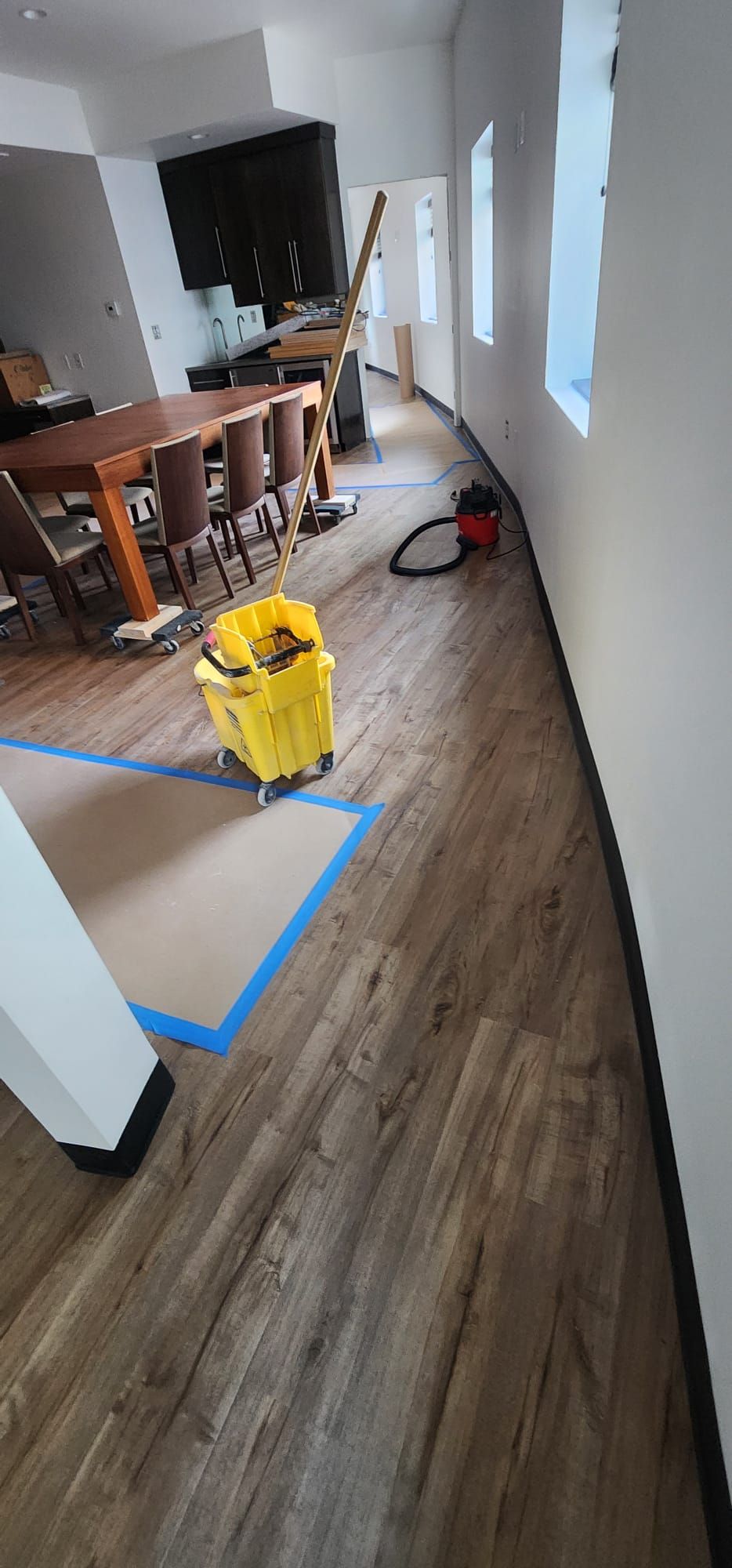 Hallway under renovation with blue tape, a yellow bucket, and tools on the floor beside a kitchen area