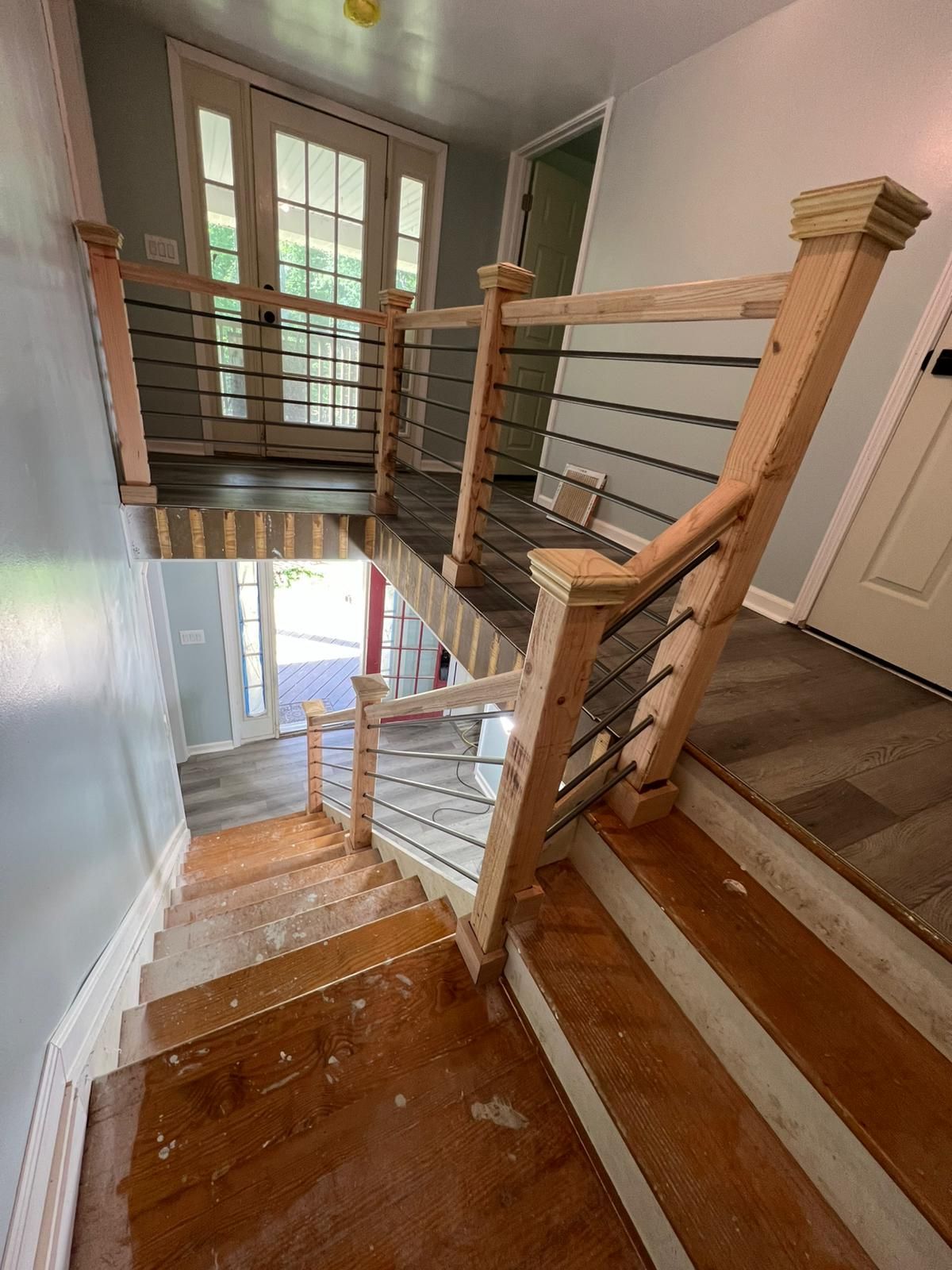 Staircase landing with wooden steps, railing, and a bright doorway below