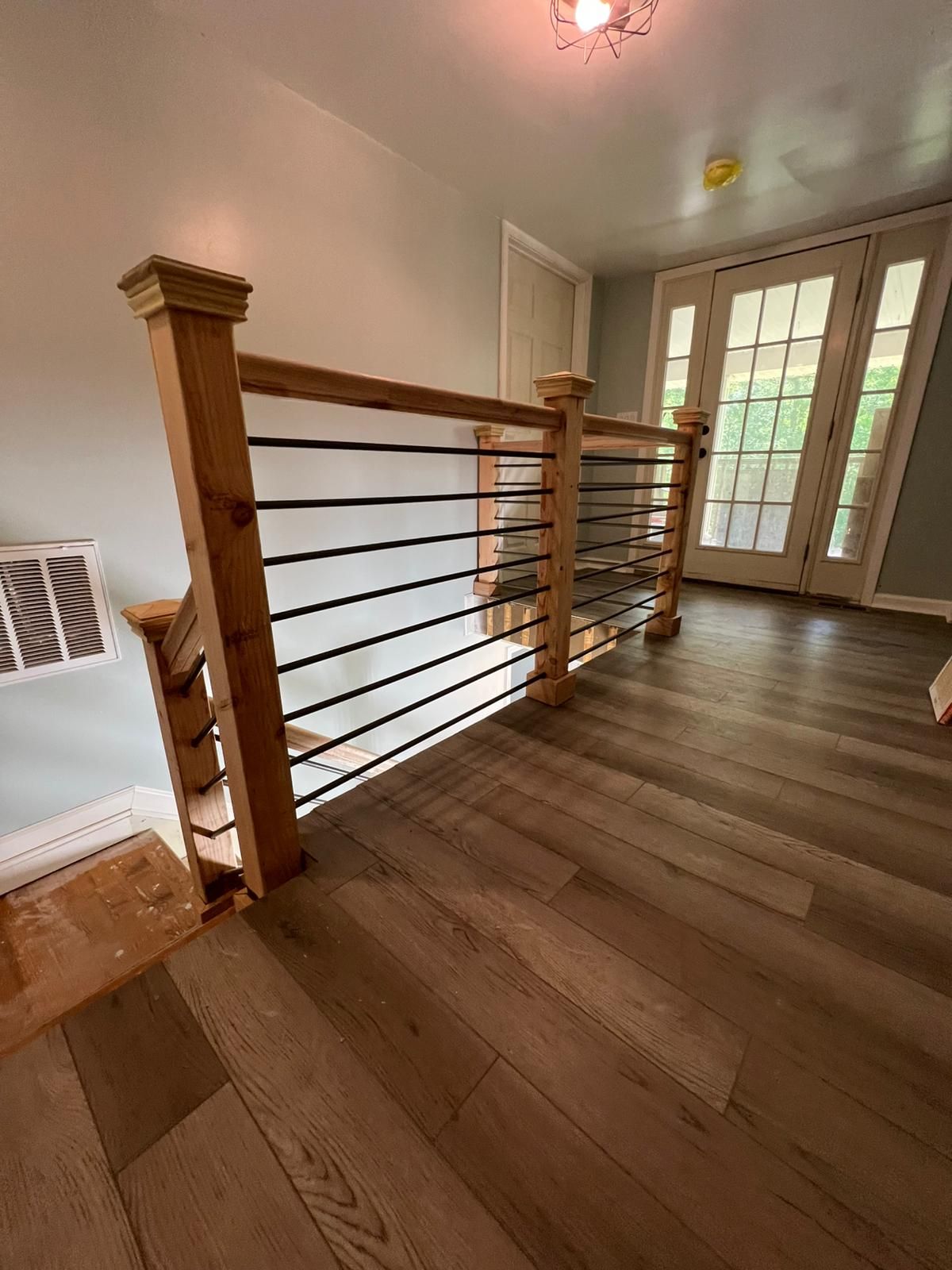 Hallway with wooden stair railing, hardwood floors, and French doors at the end