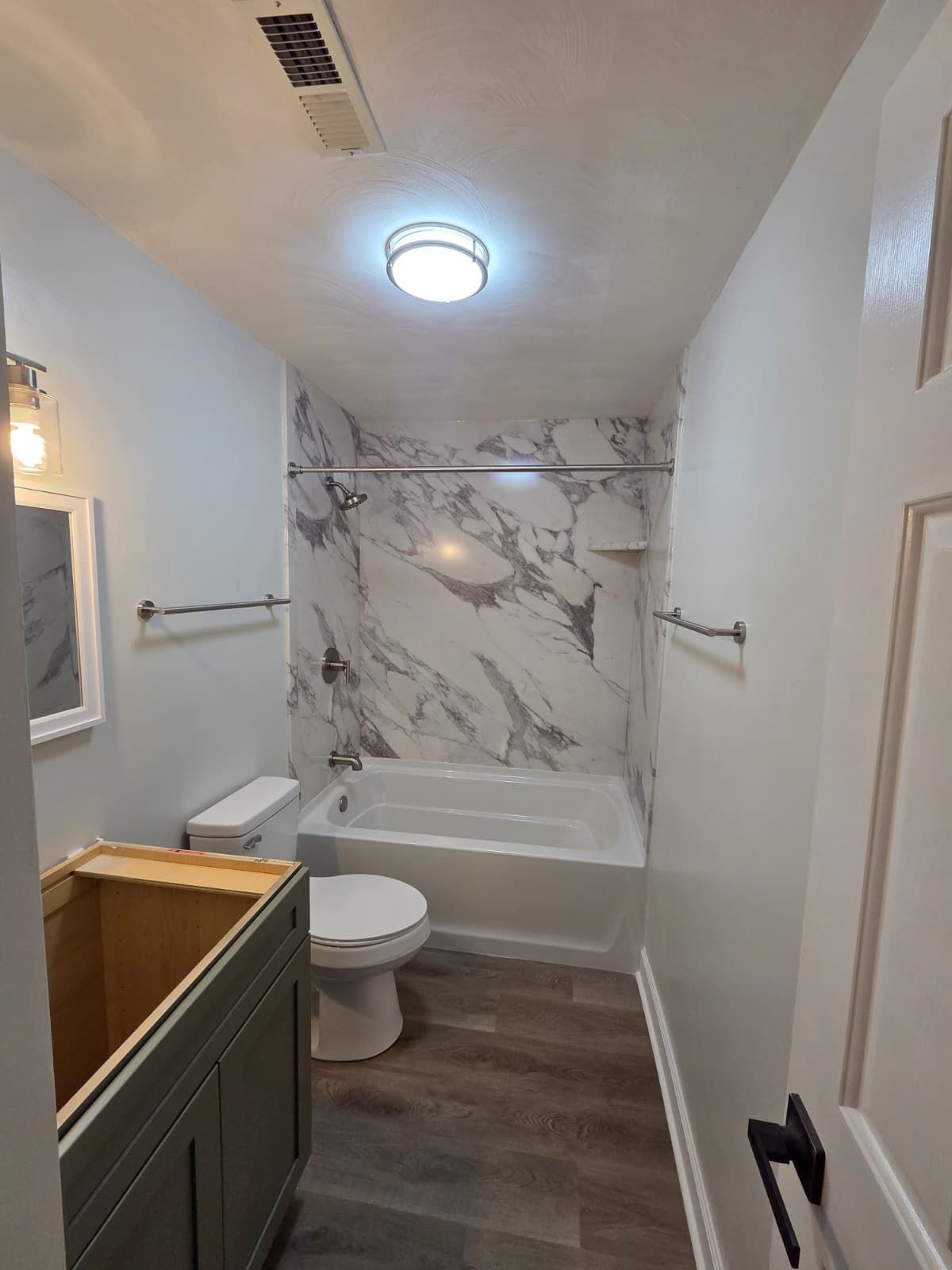Narrow bathroom with bathtub, toilet, vanity, marble shower wall, and wood-look floor
