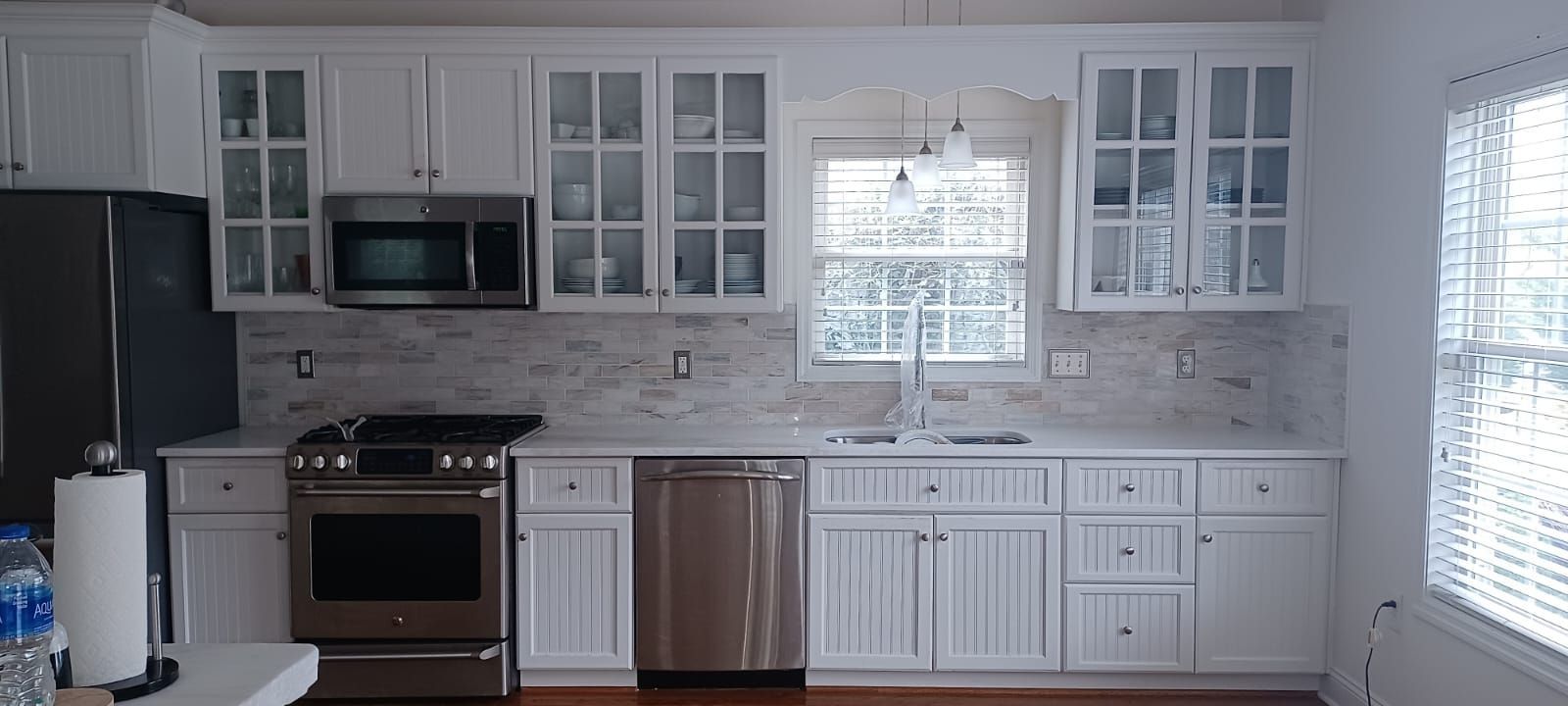 Bright white kitchen with stainless steel appliances, cabinets, and a window over the sink
