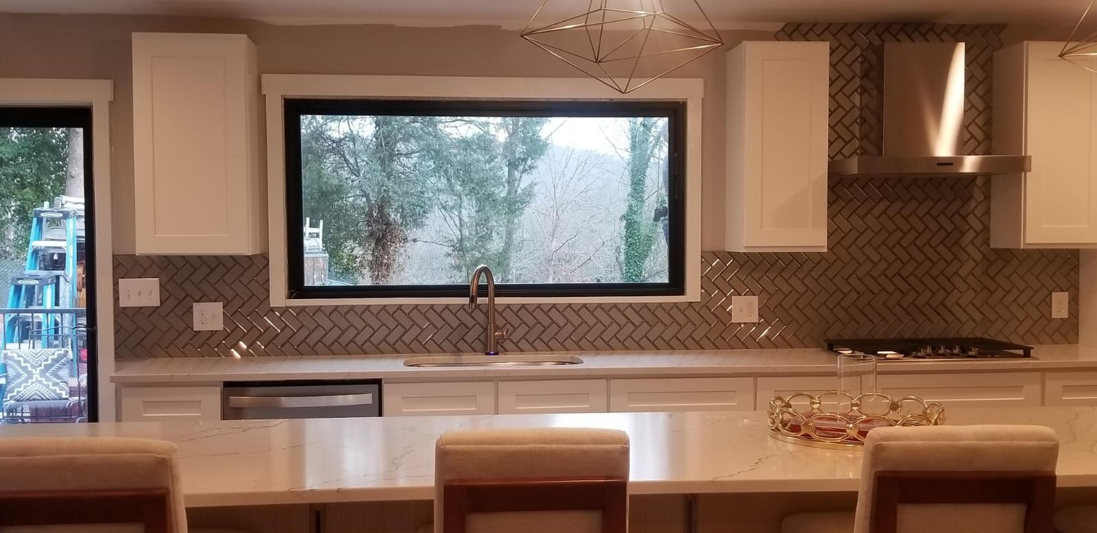Modern kitchen with white cabinets, dark tile backsplash, large window, and island with chairs