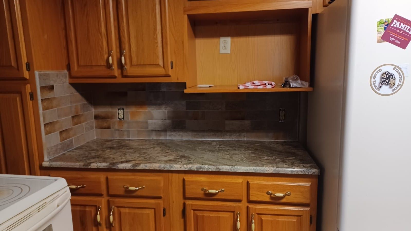 Kitchen with wooden cabinets, granite countertop, tiled backsplash, and white refrigerator.