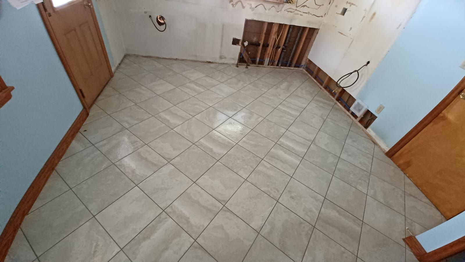 Empty tiled room with light gray floor, wooden doors, and a small cabinet along the back wall.