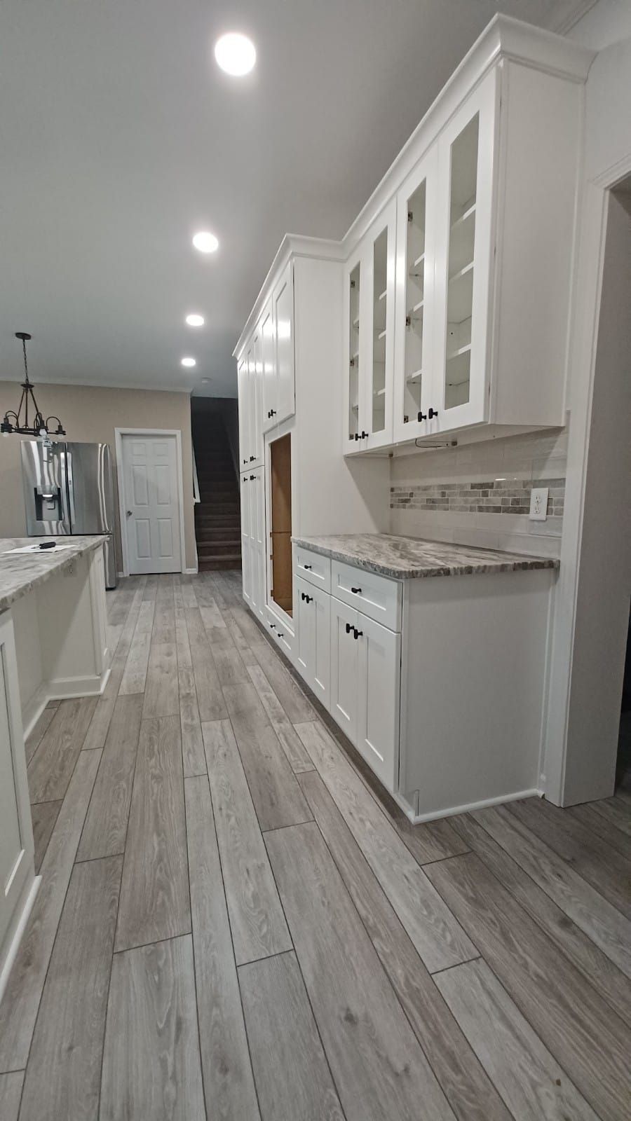 Bright modern kitchen with white cabinets, gray countertops, and light wood-look flooring.