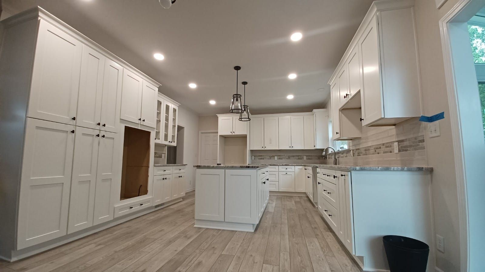Bright white modern kitchen with large cabinets, island, recessed lights, and wood-look flooring