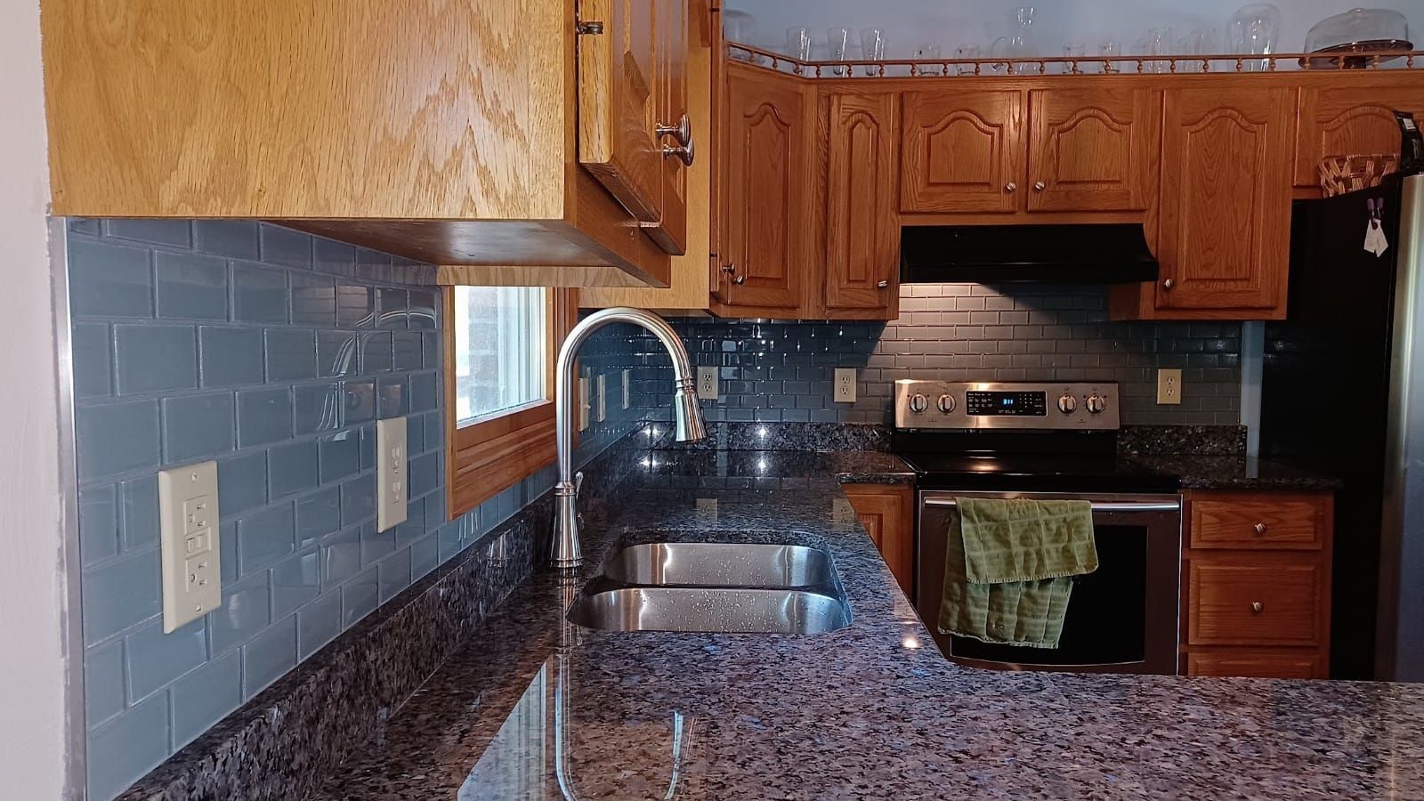 Kitchen with wood cabinets, blue tile backsplash, dark granite counters, sink, and stainless steel stove.