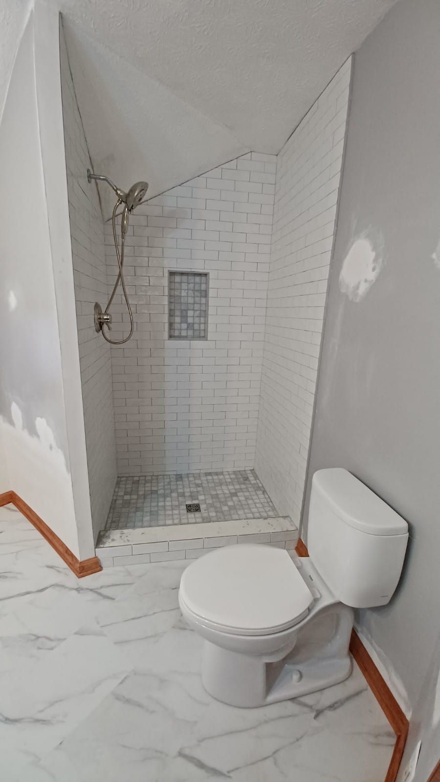 Small unfinished bathroom with a toilet and tiled shower stall under slanted walls.